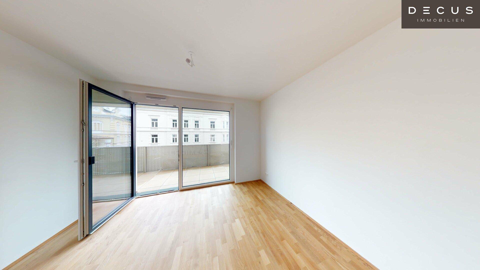 Geräumiges Zimmer mit Holzboden und großen Fenstern, die Zugang zu einem Außenbereich bieten.