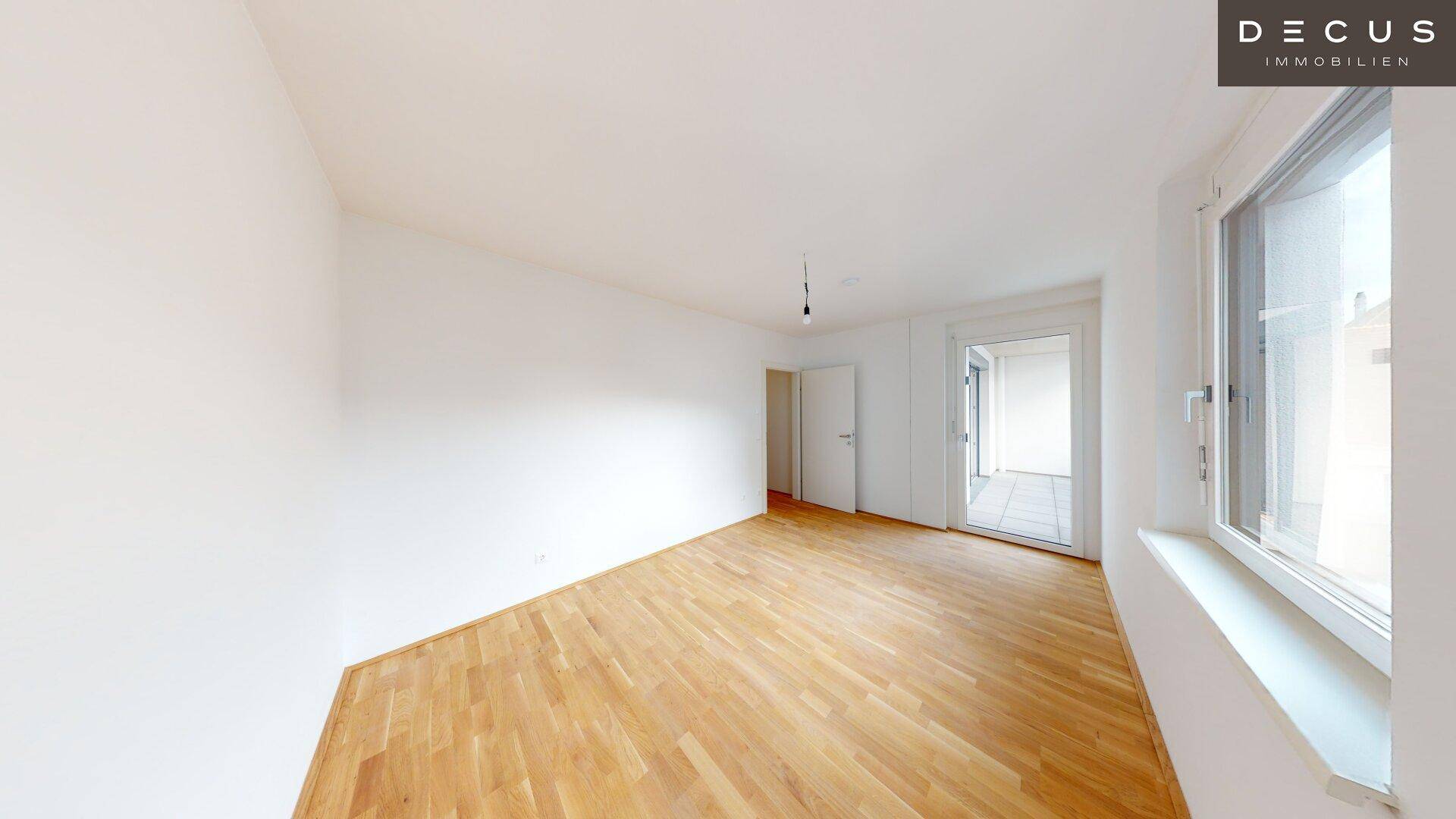 Schlafzimmer mit Holzboden und Fenster, das viel Tageslicht hereinlässt.