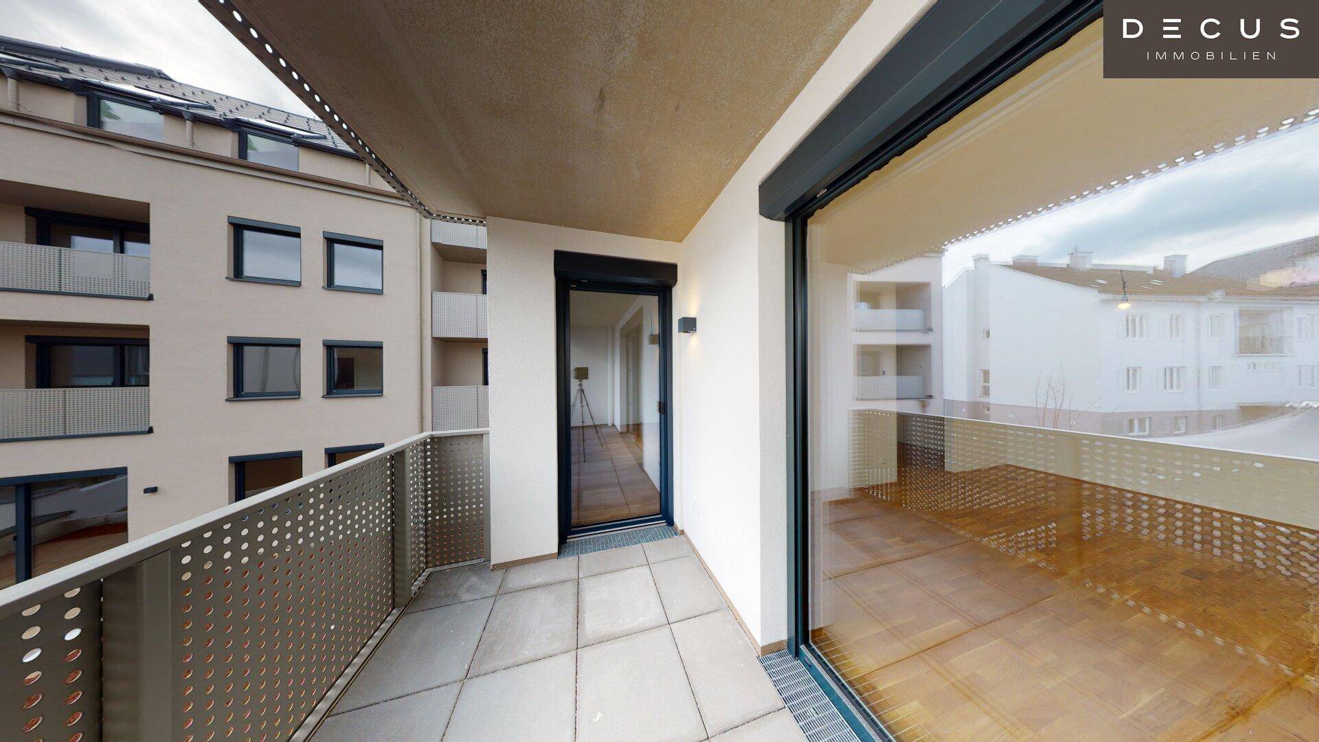 Geräumiger Balkon mit Fliesenboden und Blick auf die moderne Gebäudefassade.