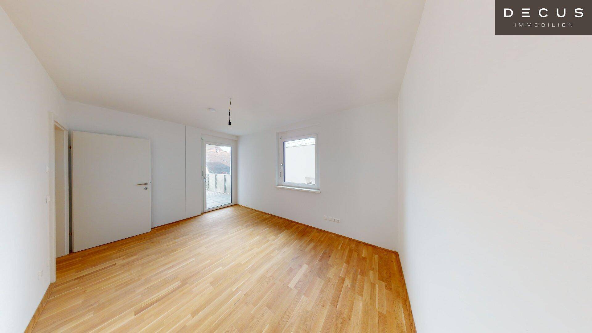 Helles Zimmer mit Parkettboden und Zugang zu einem Außenbereich oder Balkon.