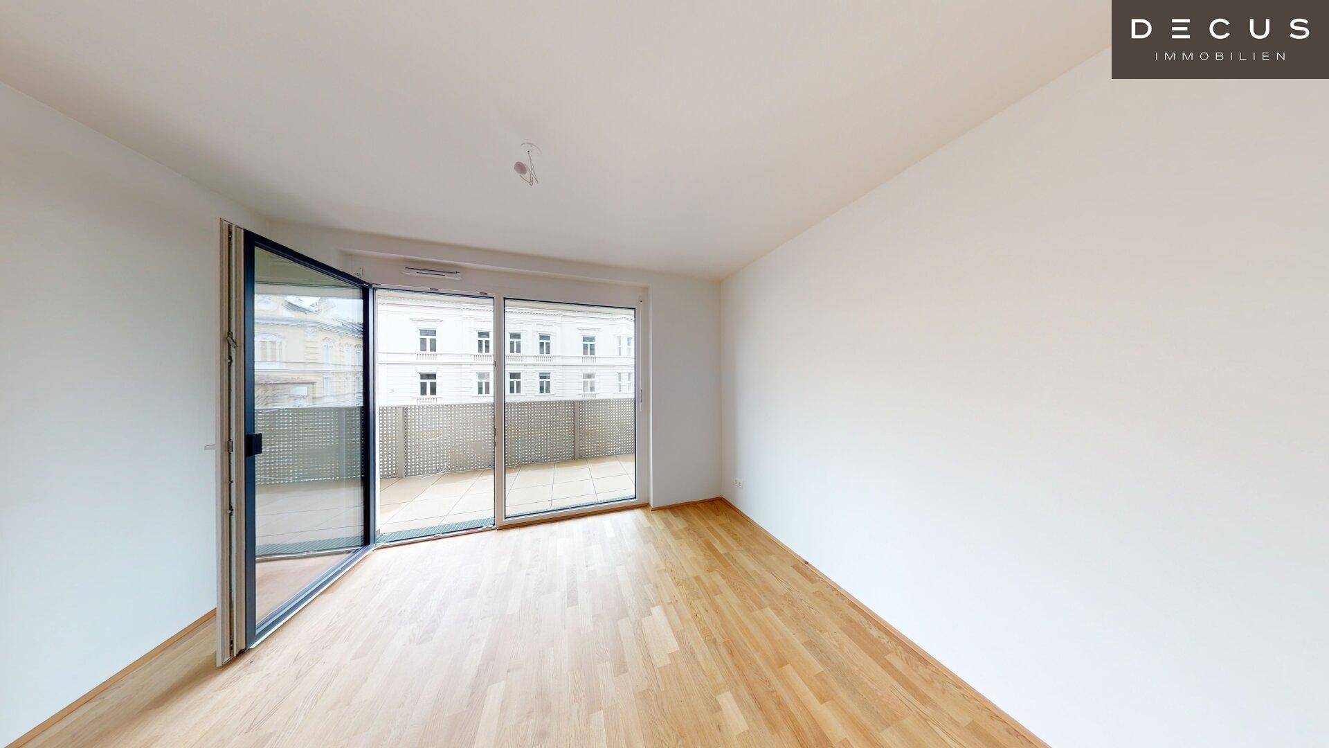 Geräumiges Zimmer mit Parkettboden und großen Fenstern zum Balkon hin.