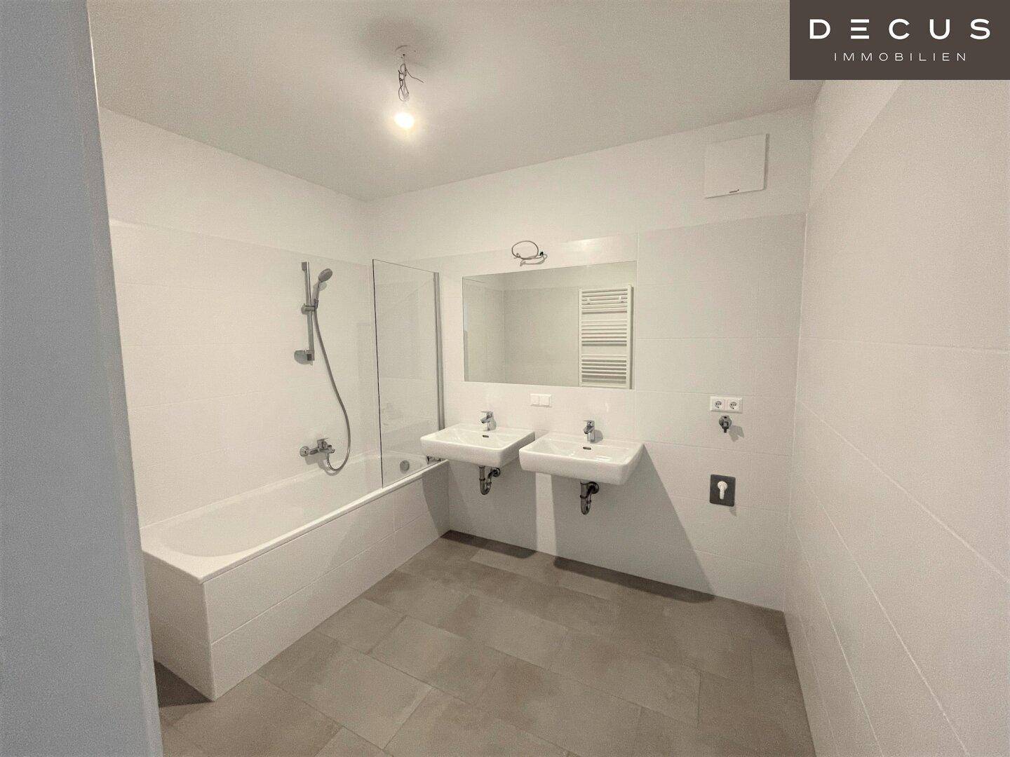 Modernes Badezimmer mit weißen Fliesen, zwei Waschbecken, Badewanne mit Duschfunktion und Handtuchheizkörper.