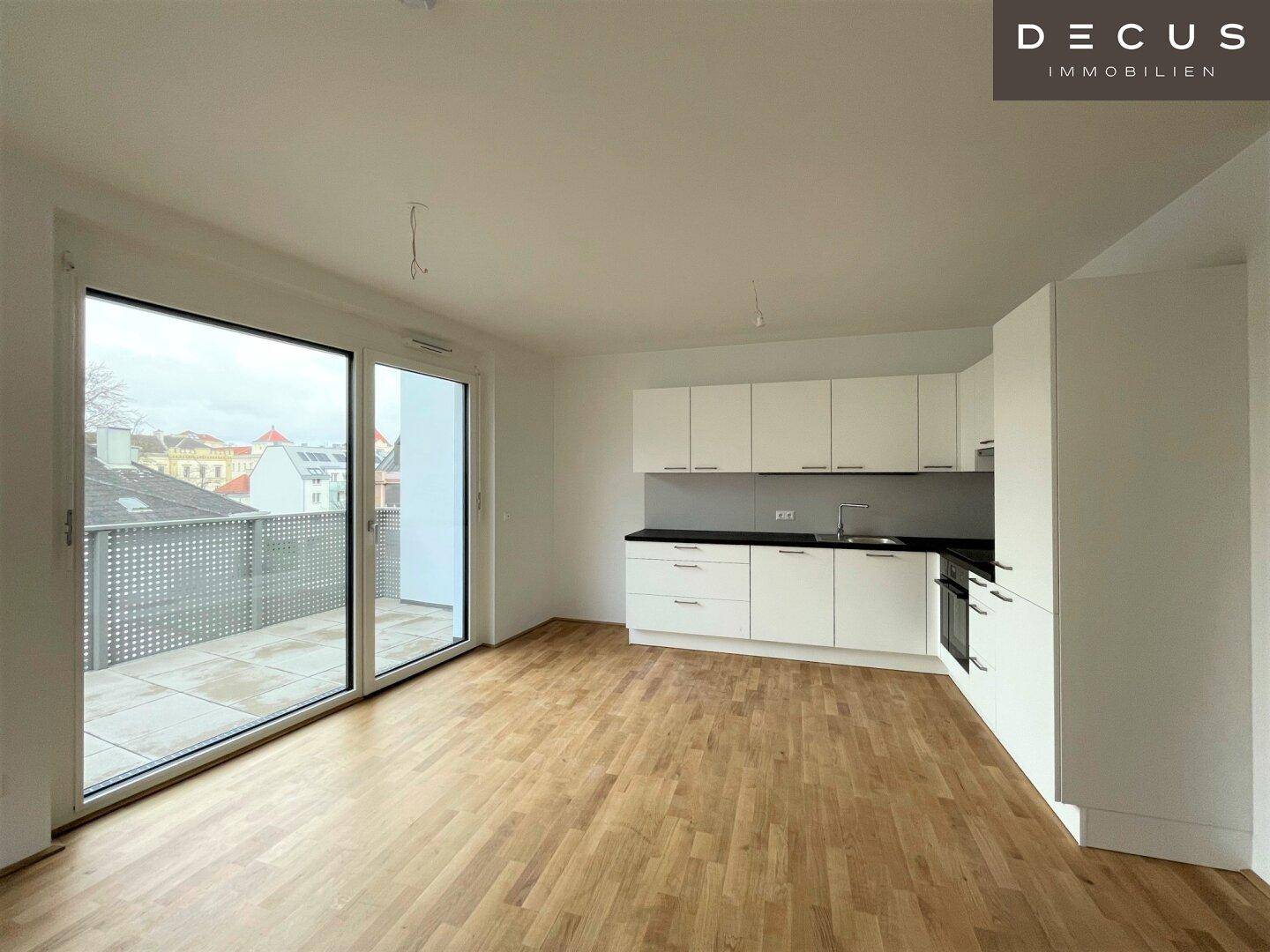 Heller offener Wohnbereich mit moderner Einbauküche, Parkettboden und Zugang zur Terrasse.