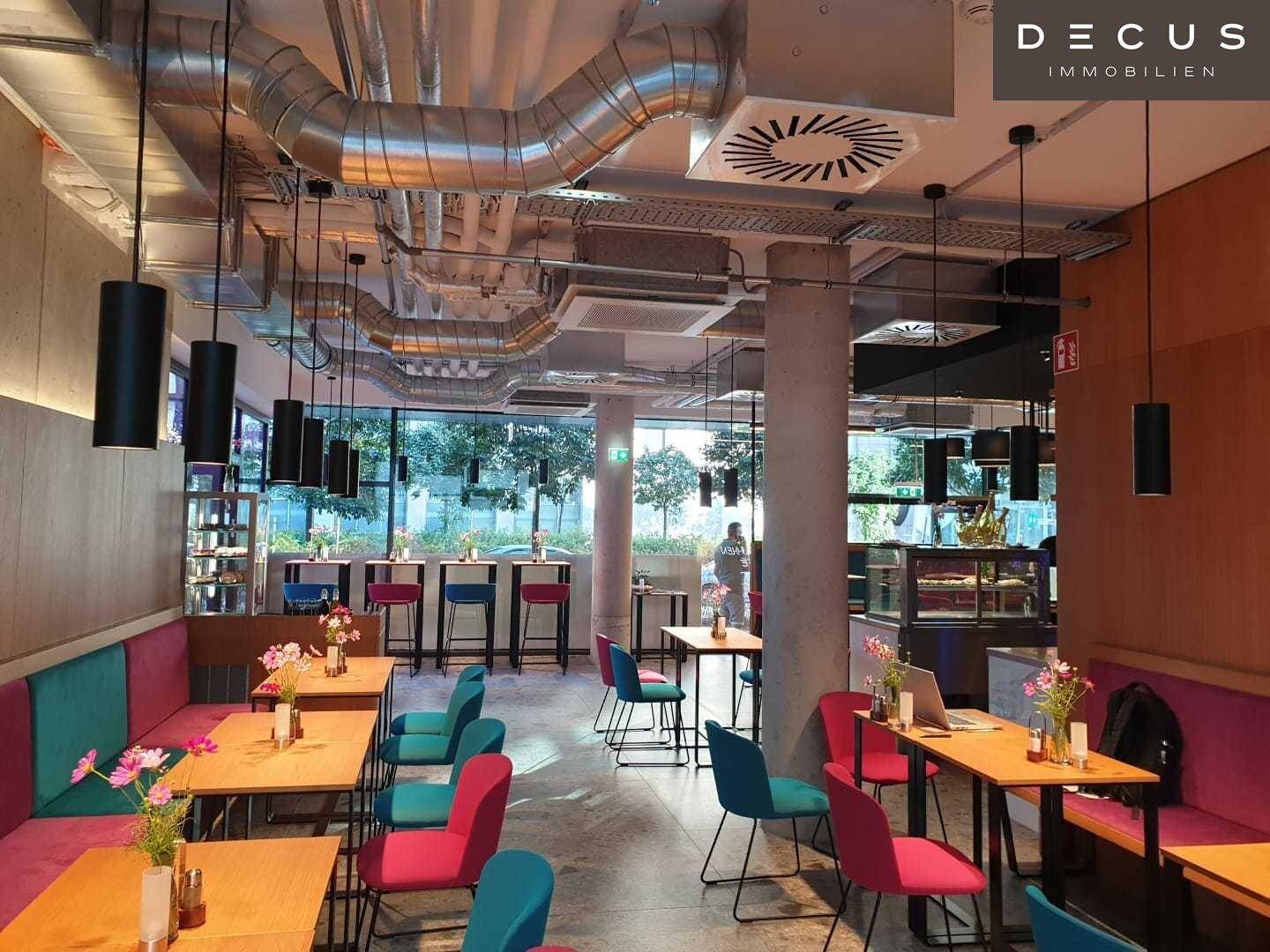 Modernes Café mit industriellem Design, sichtbaren Lüftungsrohren und farbenfrohen Sitzgelegenheiten.