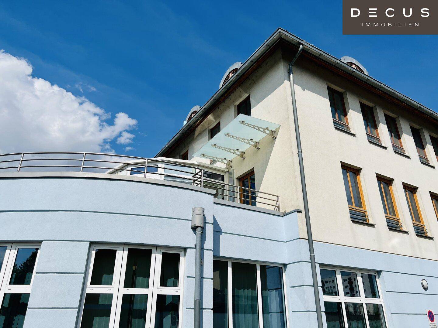 Außenansicht eines modernen Gebäudes mit blauer Fassade, großen Fenstern und einem Balkon.
