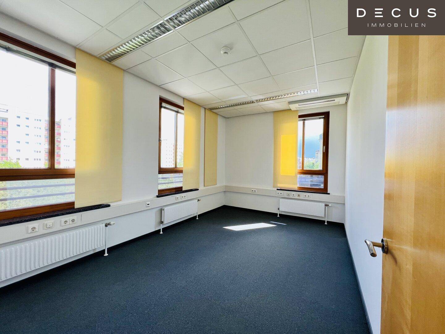Leerer Büroraum mit Teppichboden, mehreren Fenstern und gelben Rollos, bereit zur Nutzung.