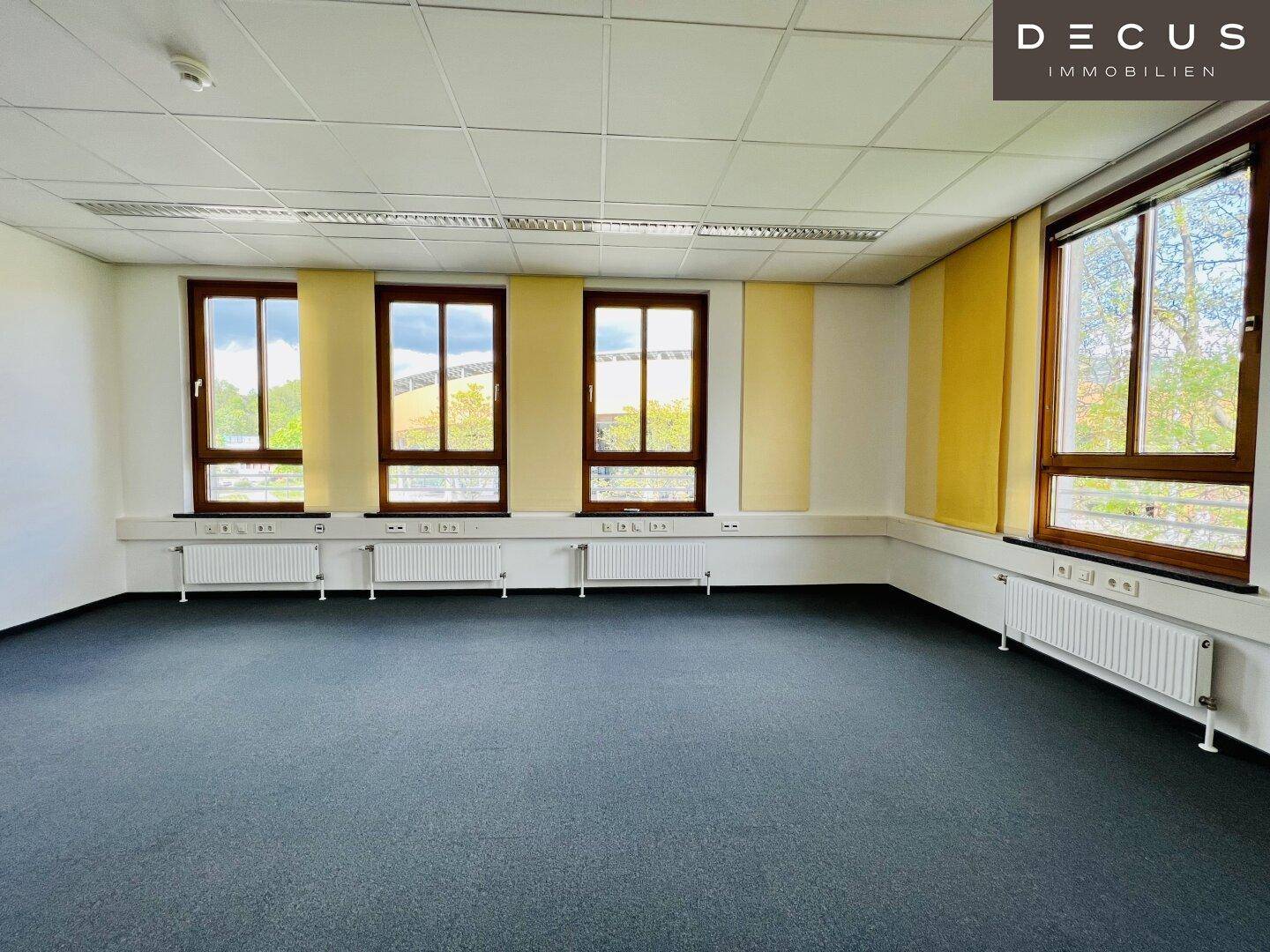 Geräumiges, leeres Büro mit Teppichboden, vielen Fenstern und gelben Rollos, bereit zur Einrichtung.