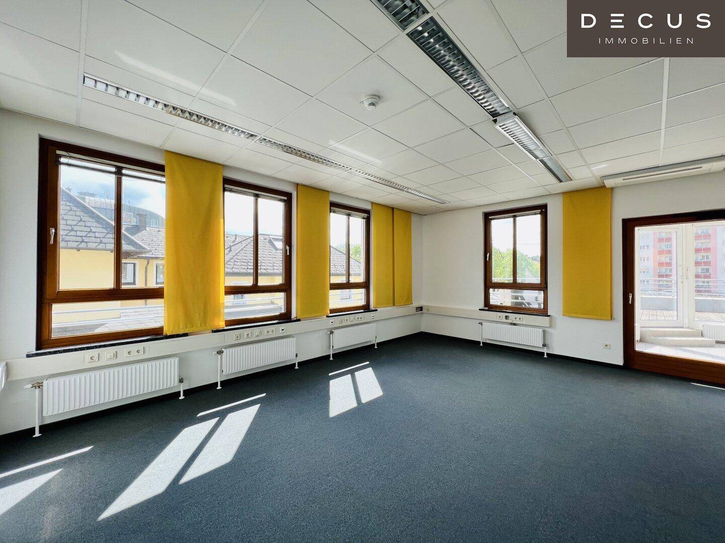 Leeres Büro mit Teppichboden, vielen Fenstern und gelben Rollos, bietet flexible Gestaltungsmöglichkeiten.