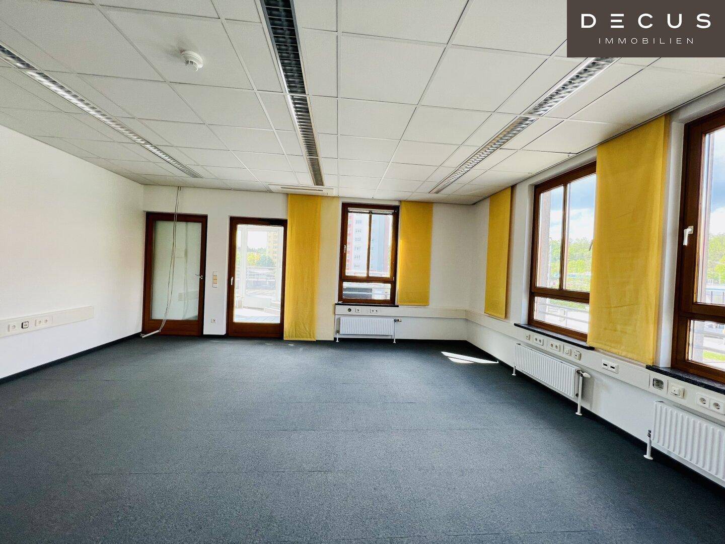 Leerer Büroraum mit Teppichboden, vielen Fenstern und gelben Rollos, ideal für individuelle Gestaltung.