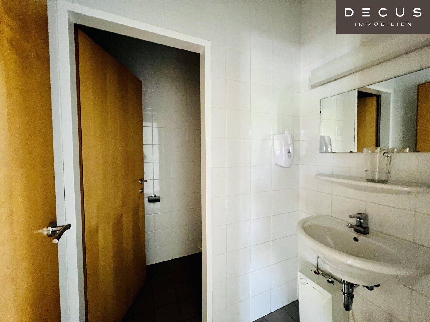 Badezimmer mit Waschbecken, Spiegel und gefliestem Duschbereich, in schlichtem und funktionalem Design.
