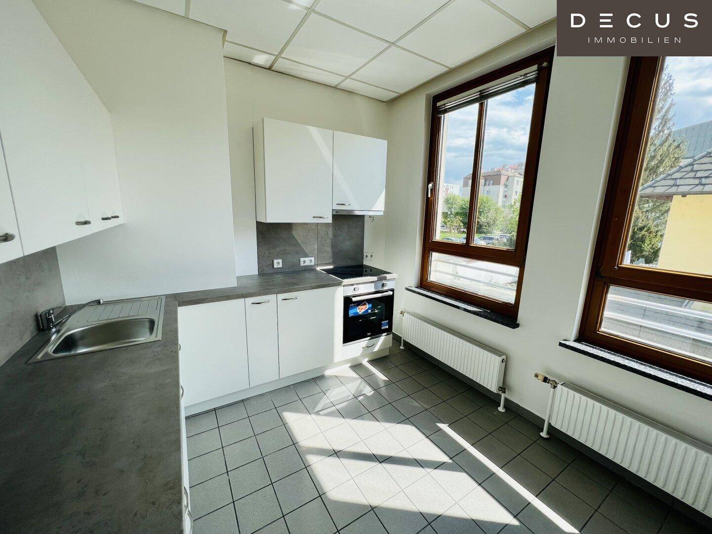 Moderne Einbauküche mit weißen Schränken, grauer Arbeitsplatte und Fliesenboden, hell und funktional.