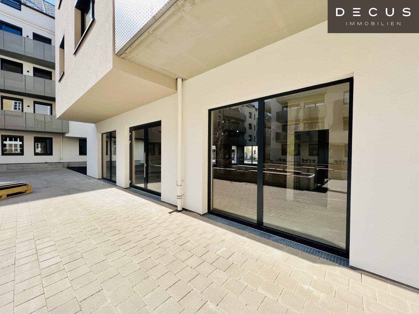 Gepflasterte Terrasse vor großen Glasfronten eines modernen Gebäudes, ideal für Außengastronomie.