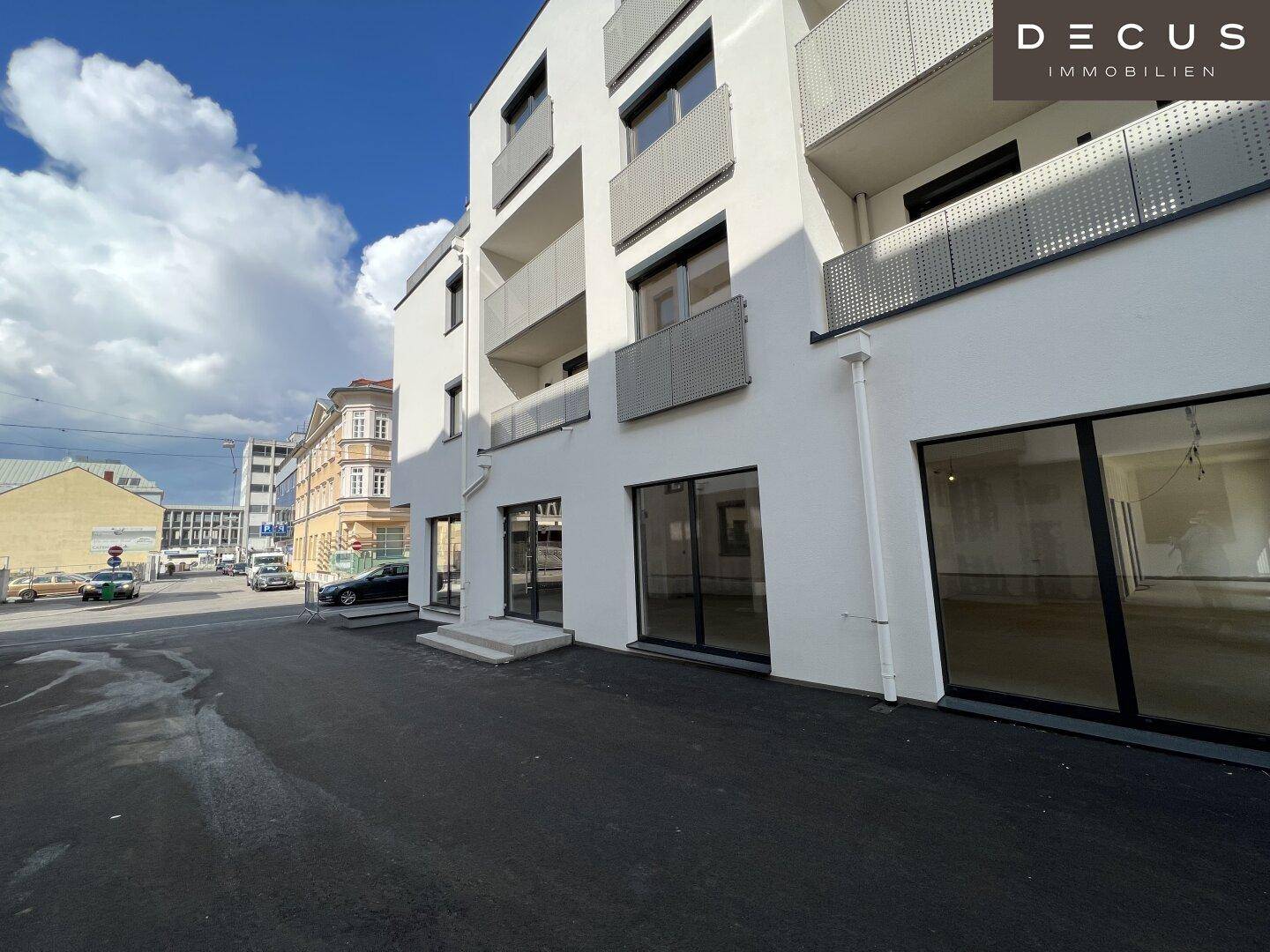 Moderne Gebäudefassade mit Balkonen und großen Schaufenstern, direkt an einer belebten Straße gelegen.