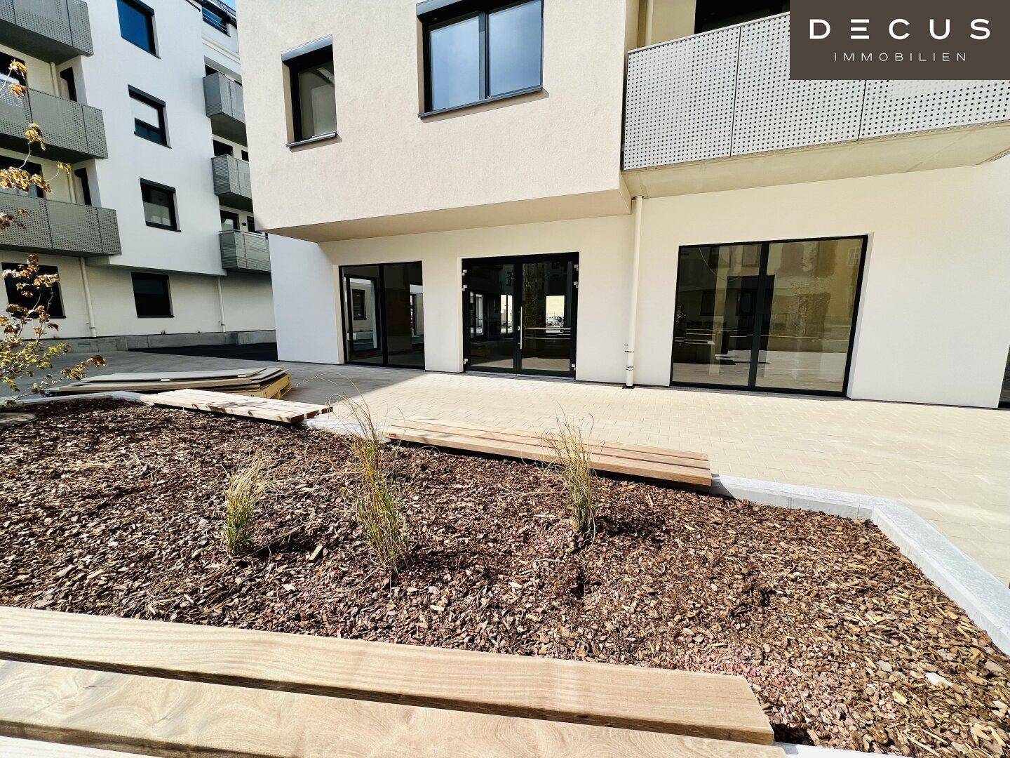 Kleiner, angelegter Gartenbereich mit Holzbänken vor den Geschäftsräumen eines modernen Gebäudes.