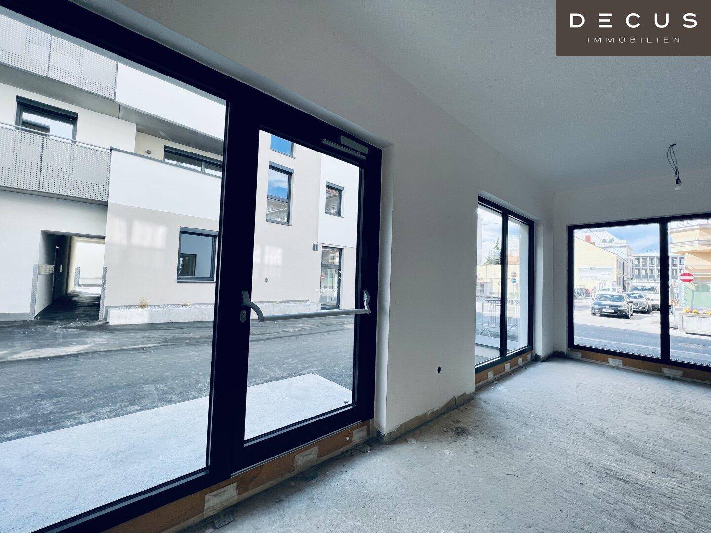 Innenansicht eines Gewerberaums mit Blick durch große Fenster auf die Straße und das moderne Gebäude.