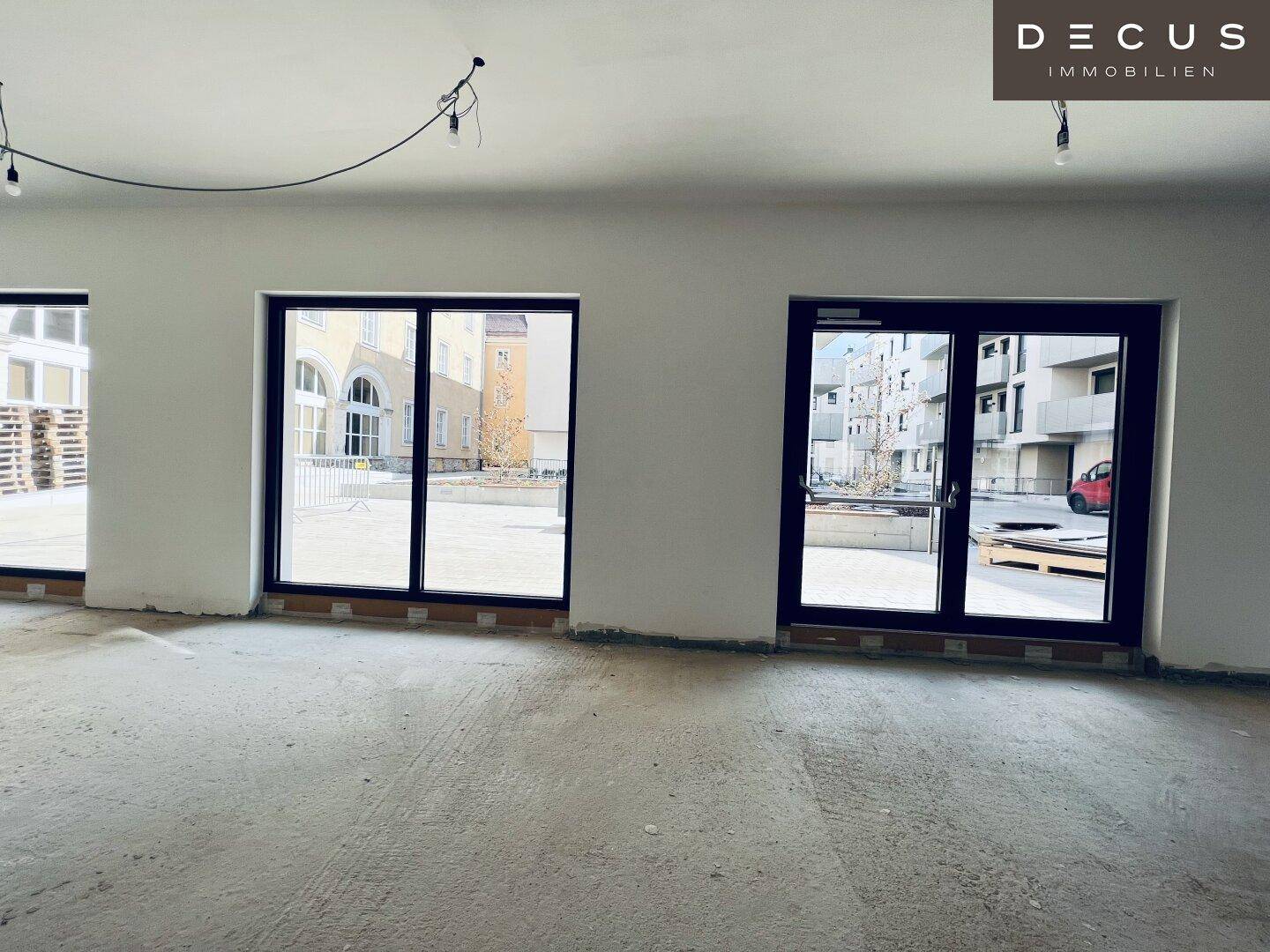 Innenansicht eines Gewerberaums mit großen Glasfronten, die auf einen gepflasterten Außenbereich blicken.
