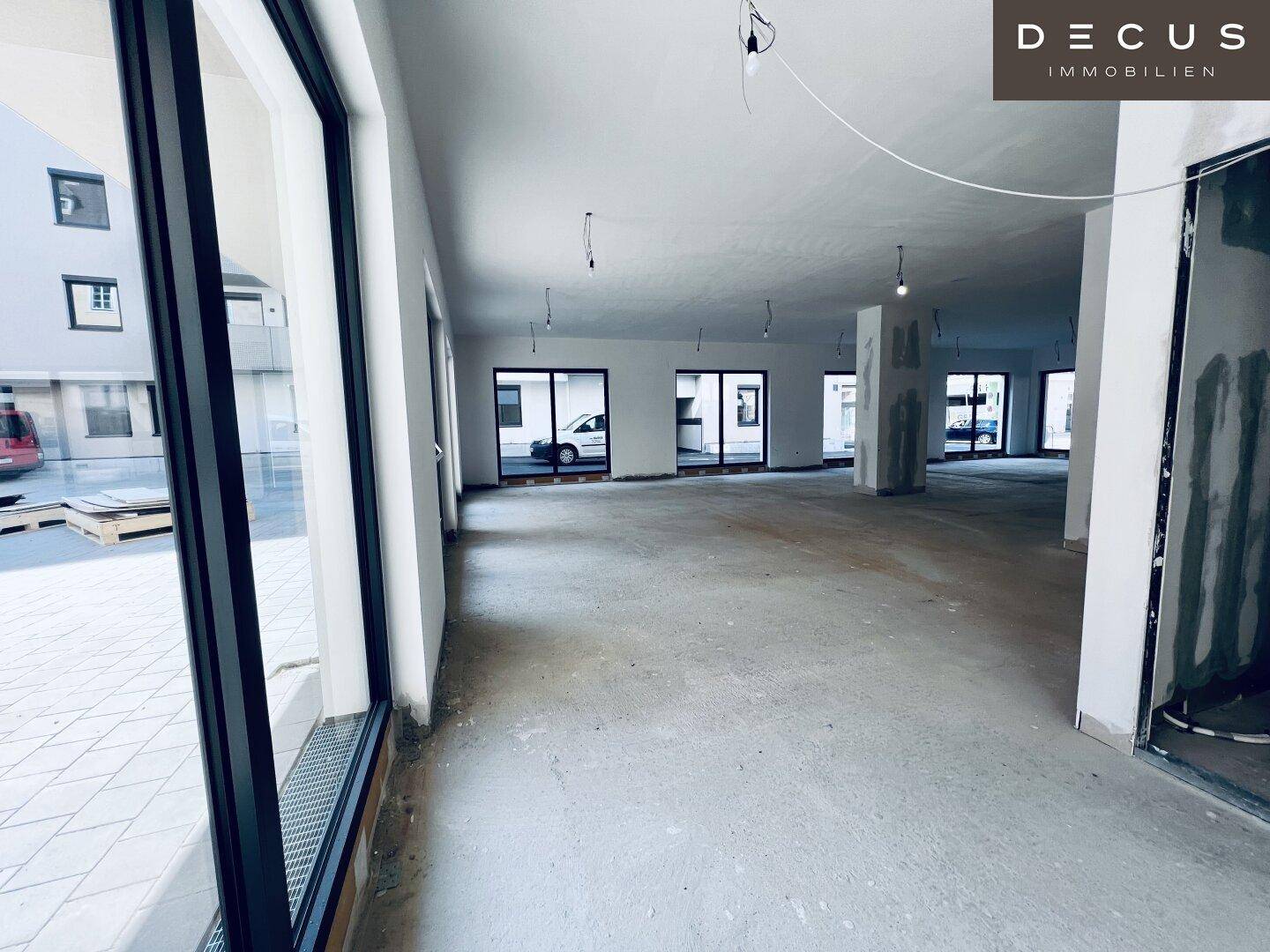 Weitläufiger Gewerberaum im Rohbau mit vielen großen Fenstern, die viel Tageslicht hereinlassen.