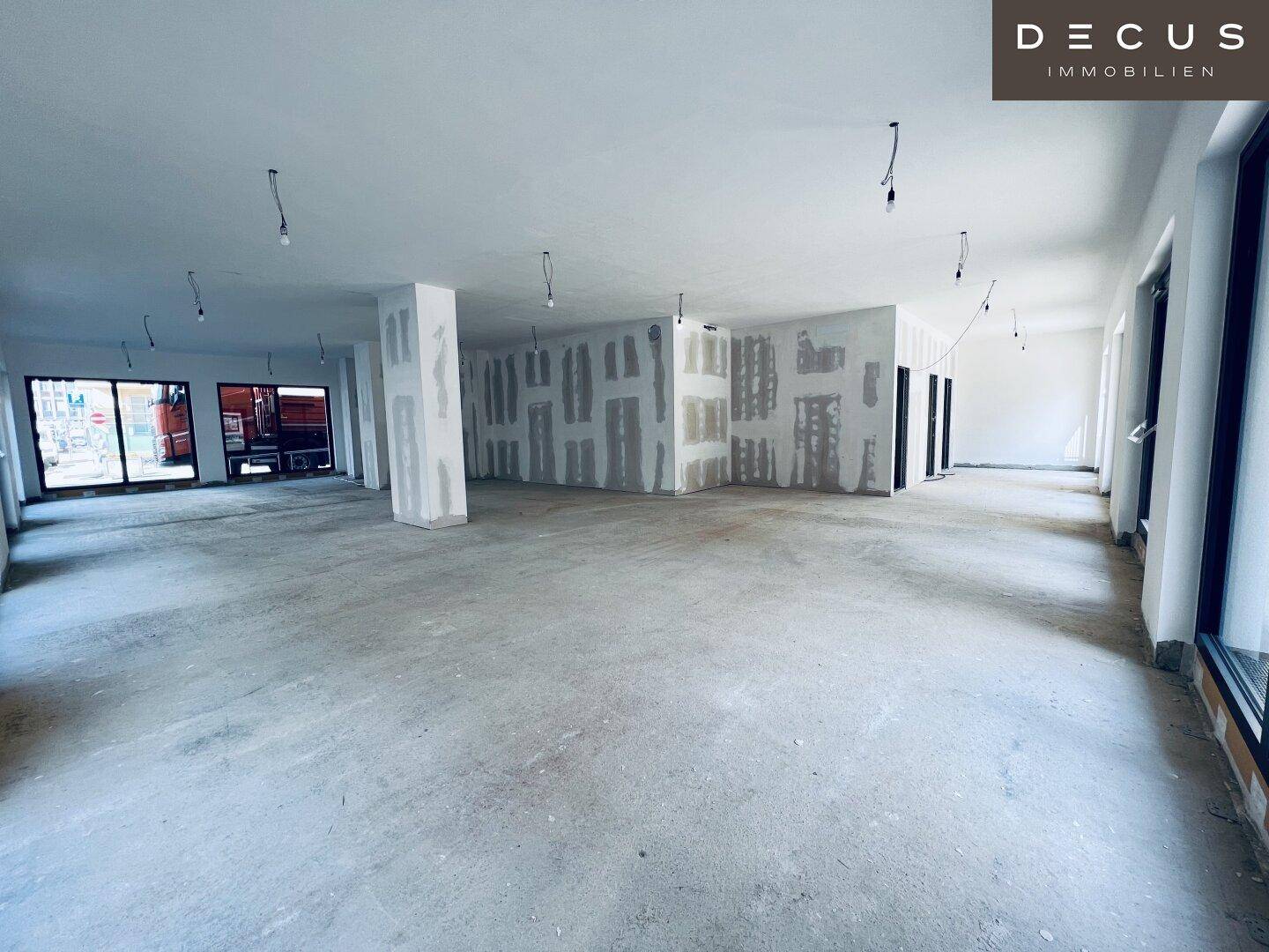Großer, offener Gewerberaum im Rohbau mit Betonboden und unfertigen Wänden, bereit für den Ausbau.