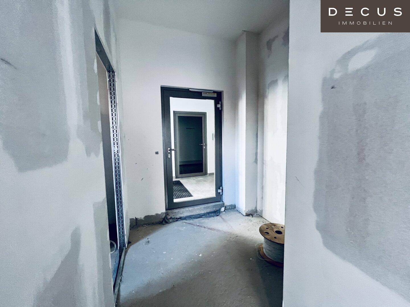 Eingangsbereich oder Flur im Rohbau mit einer modernen Tür und unfertigen Wänden.