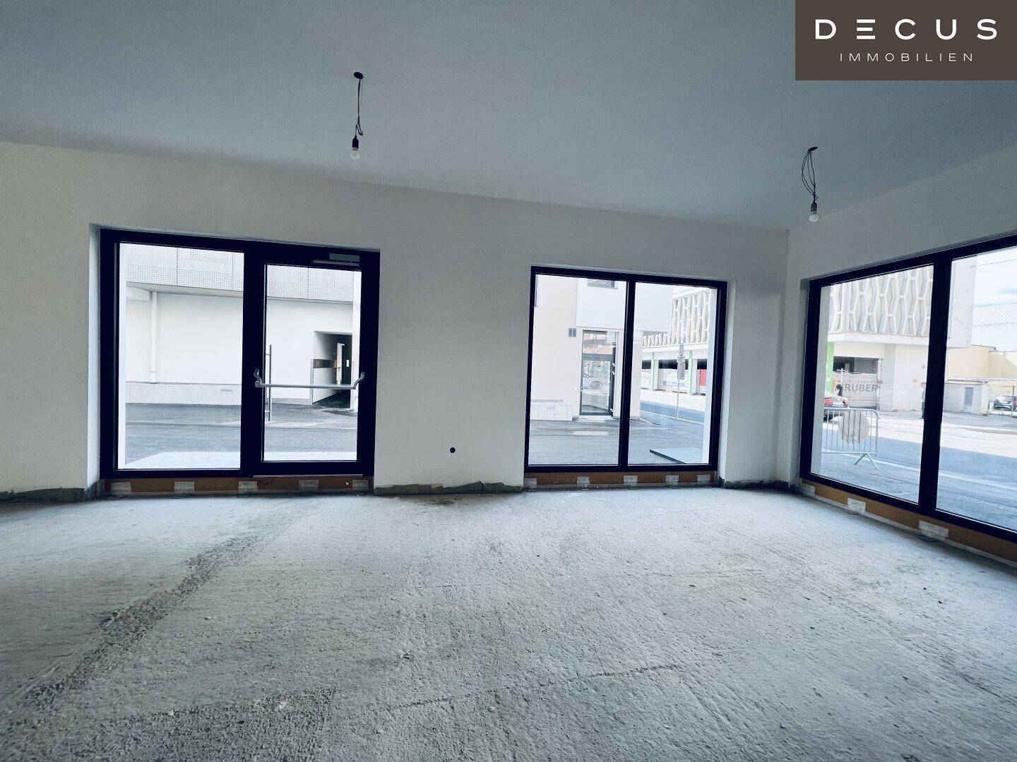 Heller Gewerberaum im Rohbau mit großen Fensterfronten und Glastüren, die viel Licht spenden.