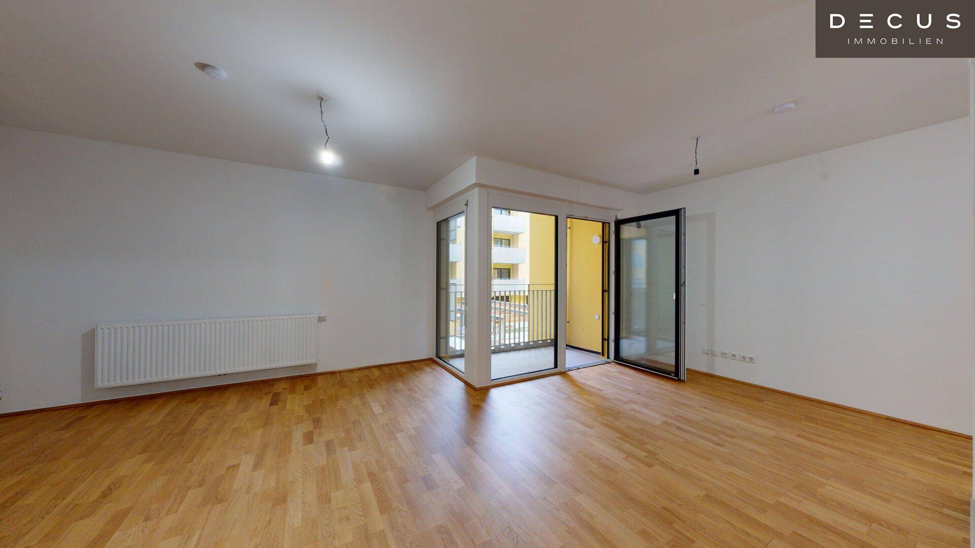 Lichtdurchfluteter Wohnbereich mit Parkettboden und großen Fenstern zum Balkon.