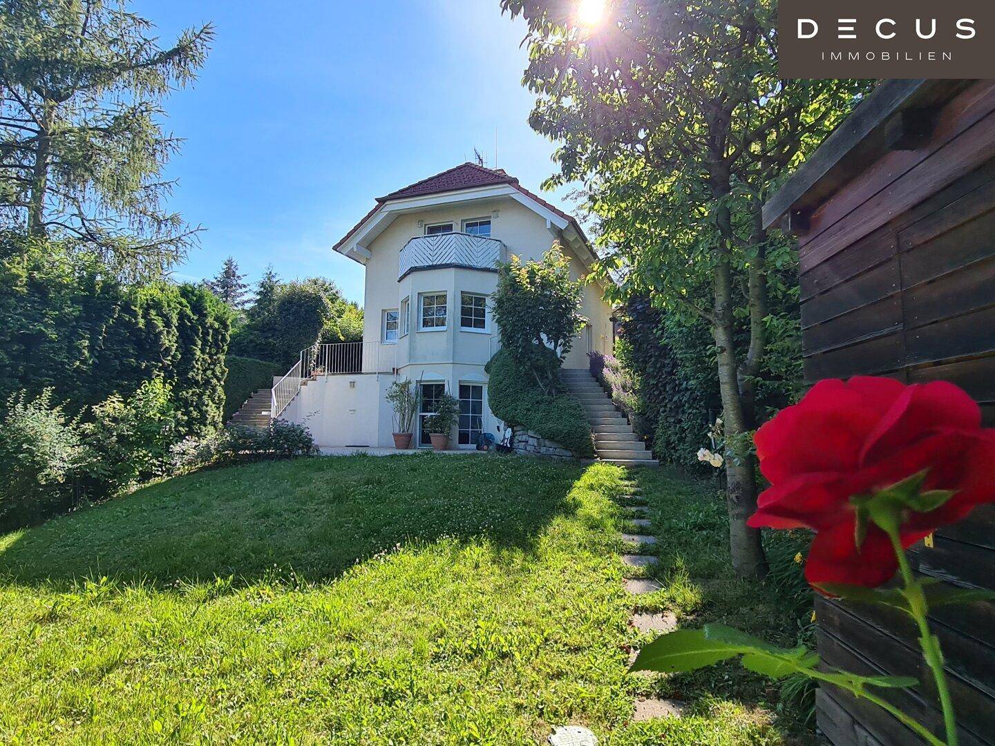 Gepflegter Gartenbereich mit Rasenfläche, altem Baumbestand und Zugang zum Haus über Treppen.