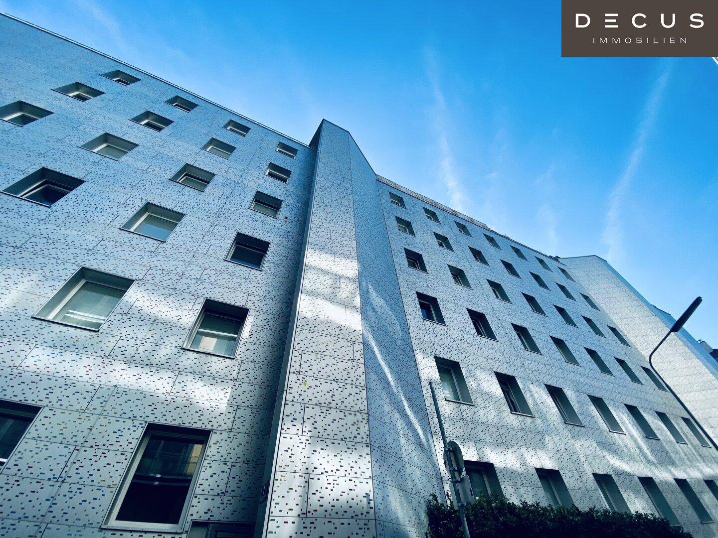 Ansicht der modernen Gebäudefassade mit zahlreichen Fenstern und einem klaren blauen Himmel.