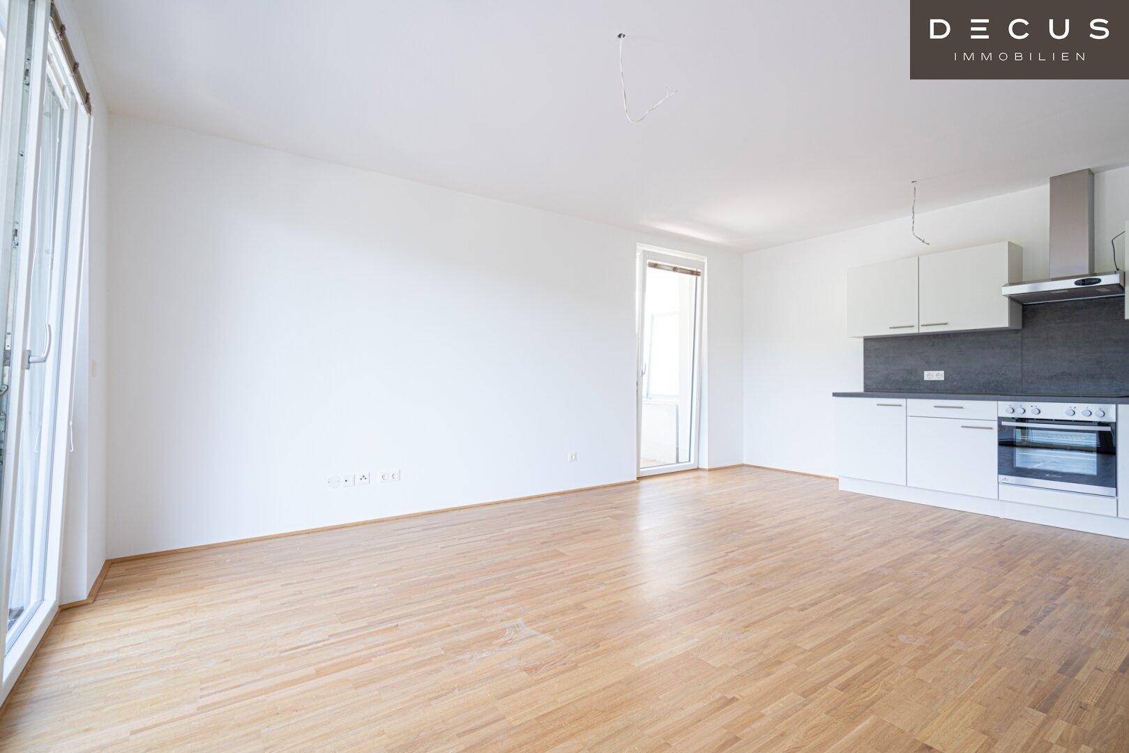 Geräumiger, heller Wohnbereich mit offener Küche, Holzboden und großen Fenstern für viel Tageslicht.