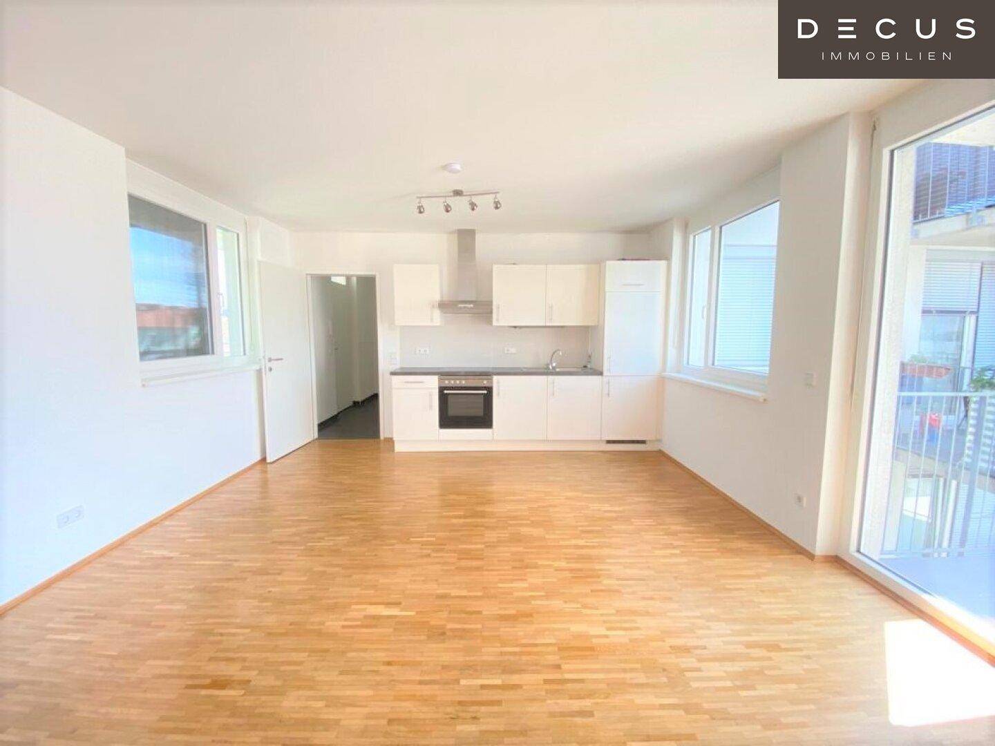 Geräumiger Wohnbereich mit offener Küche, Parkettboden und Zugang zu einem Außenbereich.