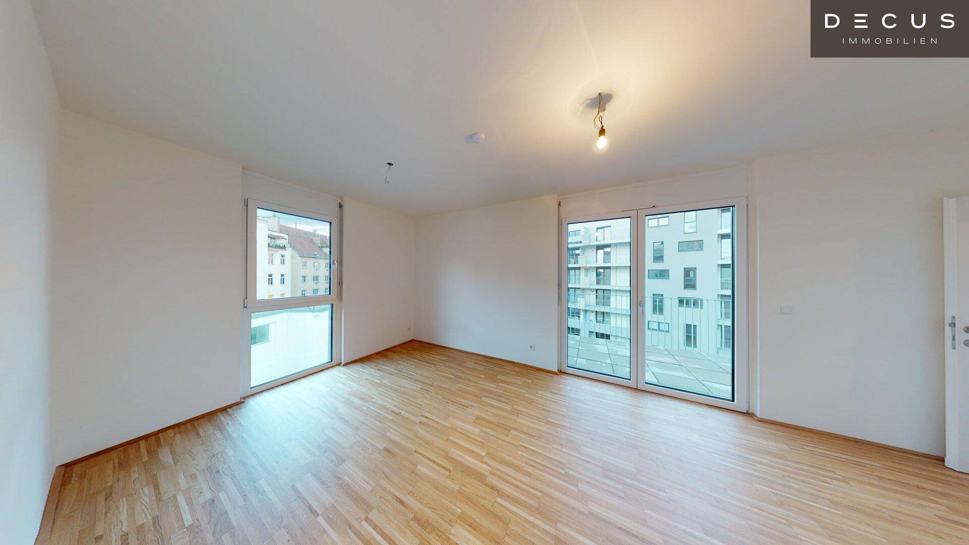 Geräumiges, leeres Zimmer mit Parkettboden und großen Fenstern, die viel Tageslicht hereinlassen.