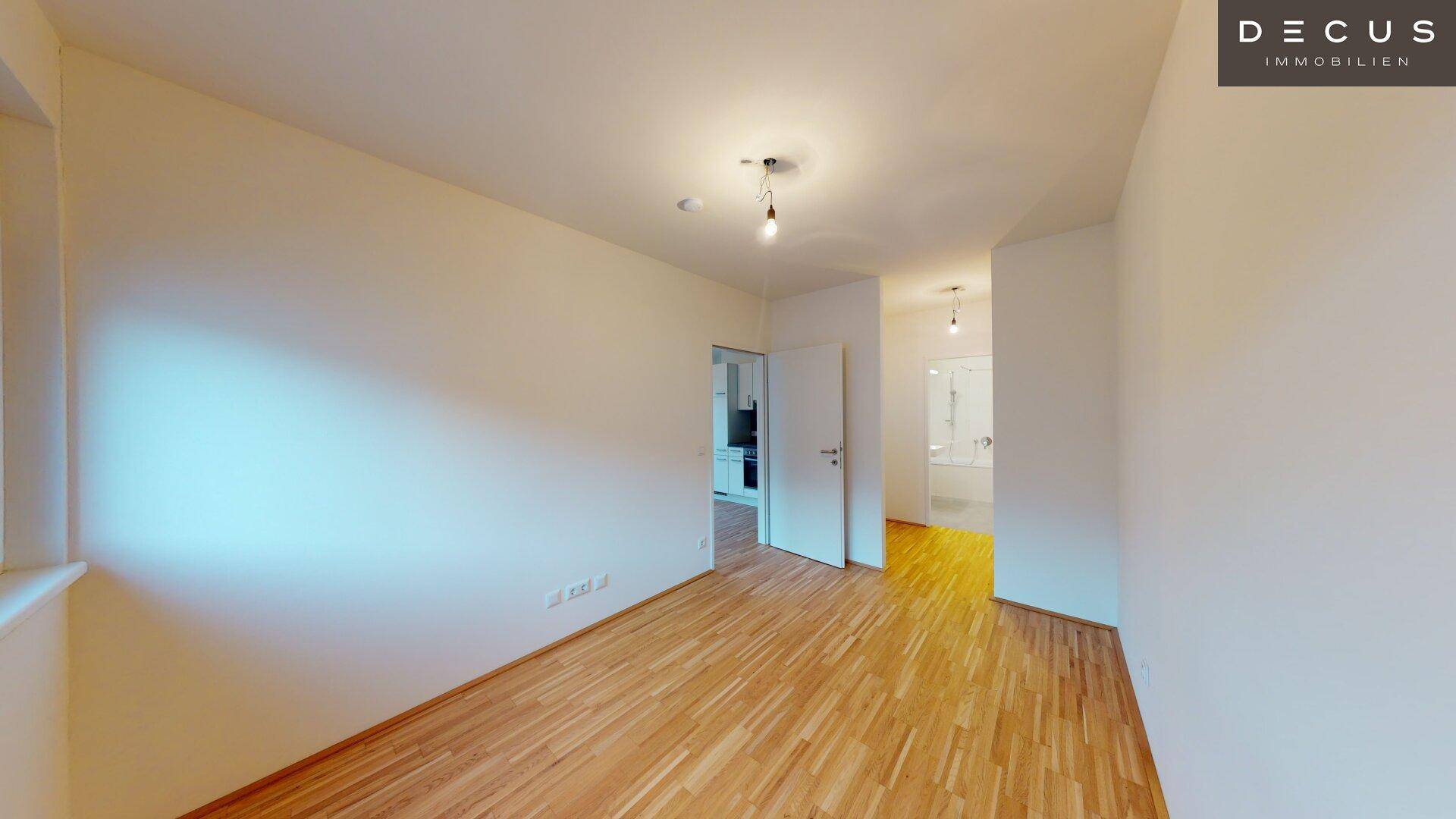 Helles Zimmer mit Parkettboden und Blick auf ein angrenzendes Badezimmer mit Badewanne.