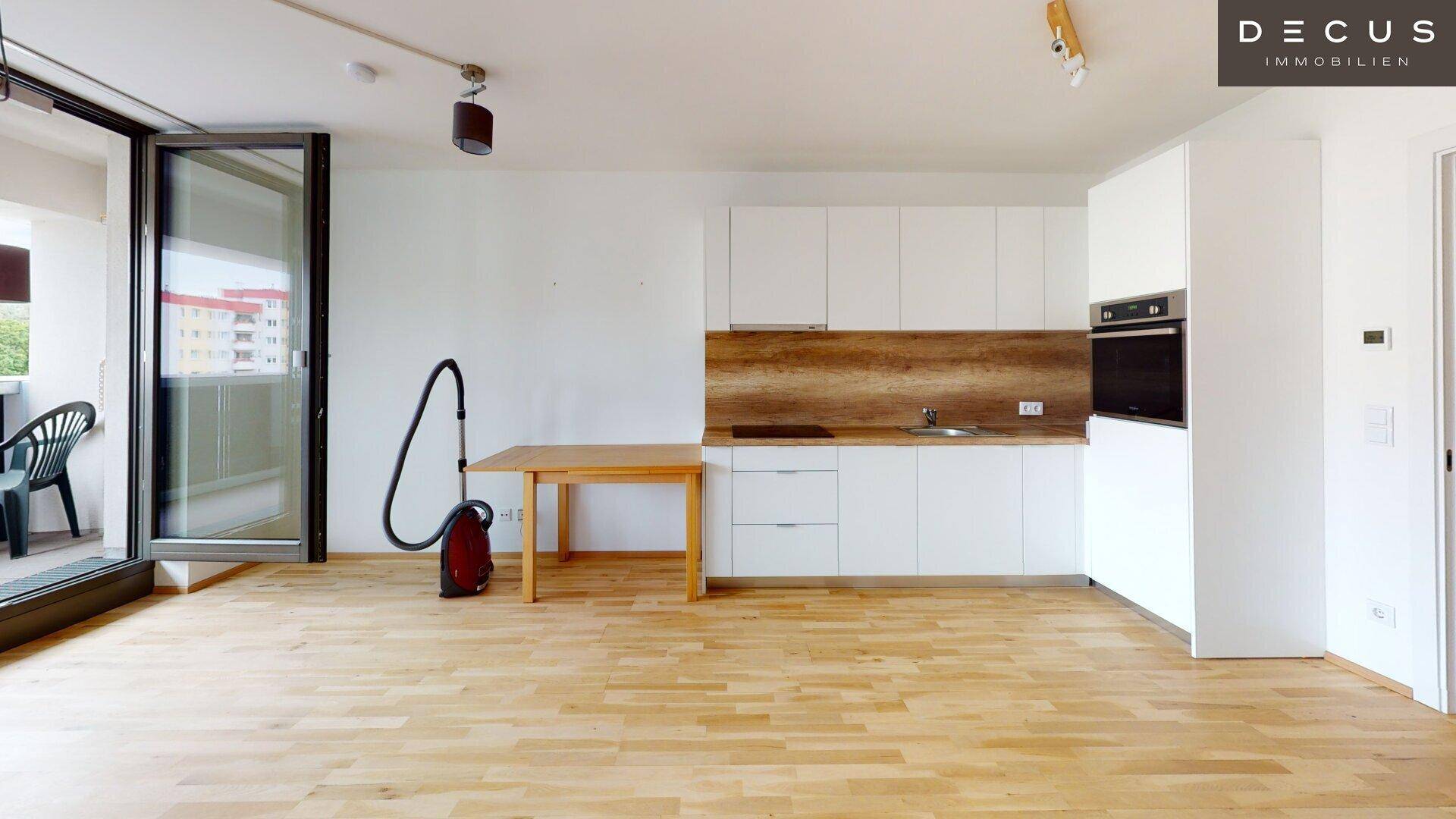 Offene Küche mit weißen Schränken, Holzarbeitsplatte und Zugang zum Balkon.