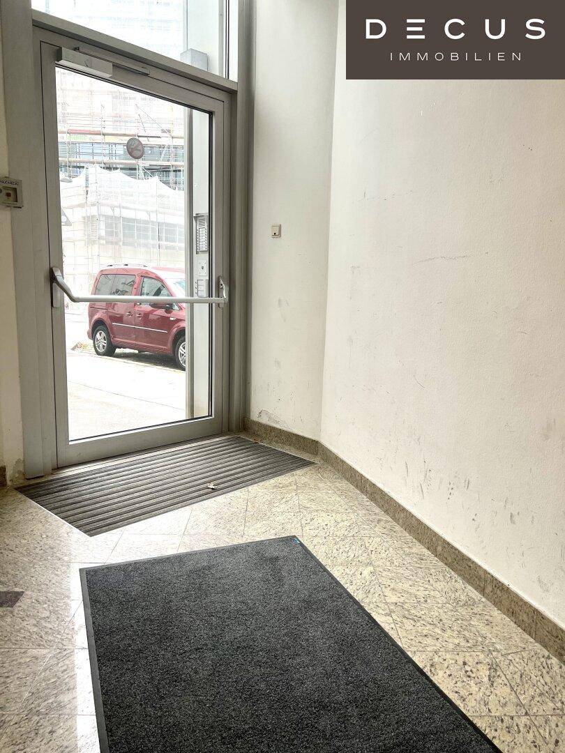 Eingangsbereich mit Glastür und Fliesenboden, führt direkt zur Straße mit einem roten Auto.