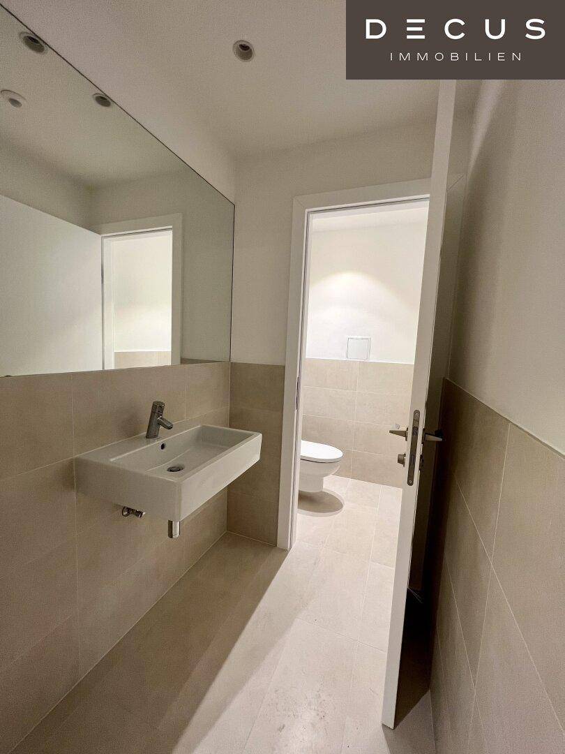 Modernes Gäste-WC mit Wandwaschbecken und großem Spiegel, in hellen Beigetönen gehalten.