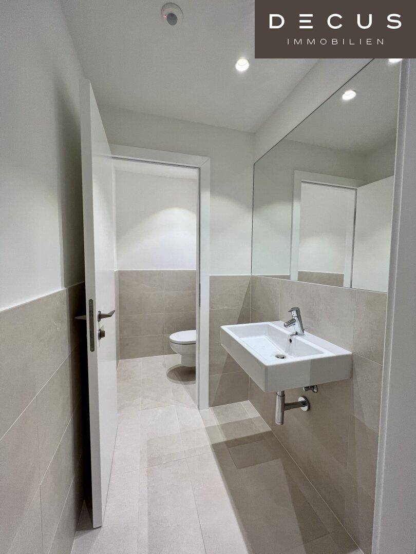 Helles Gäste-WC mit modernem Design, Wandwaschbecken und großem Wandspiegel.
