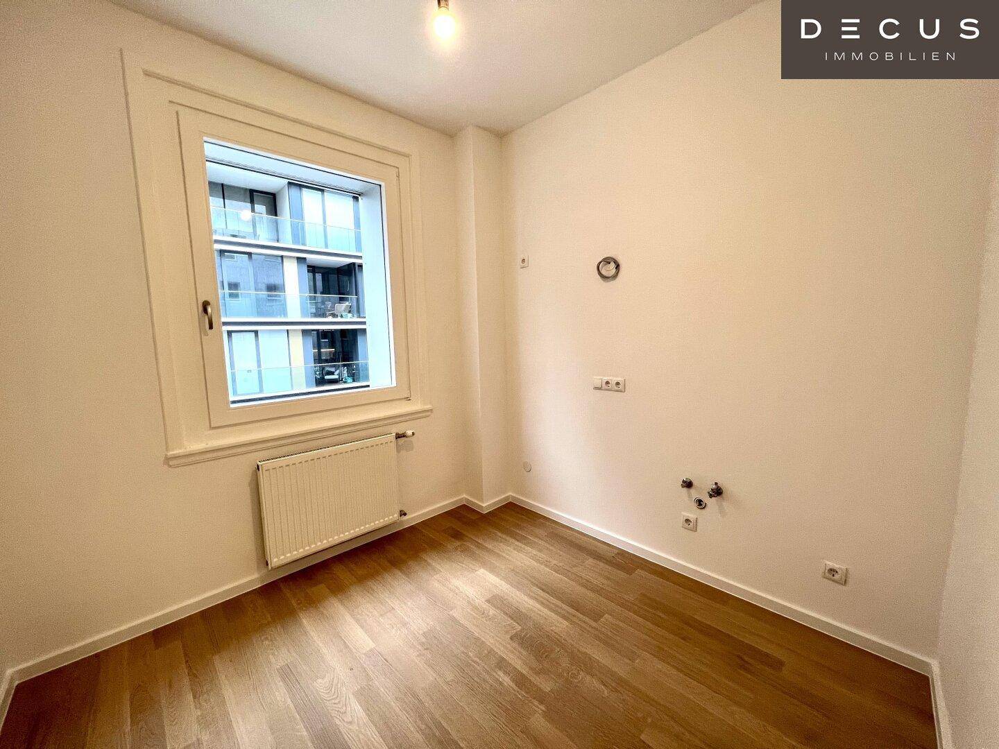 Kleiner Raum mit Fenster und Anschlüssen, vielseitig nutzbar, mit Blick auf moderne Gebäude.