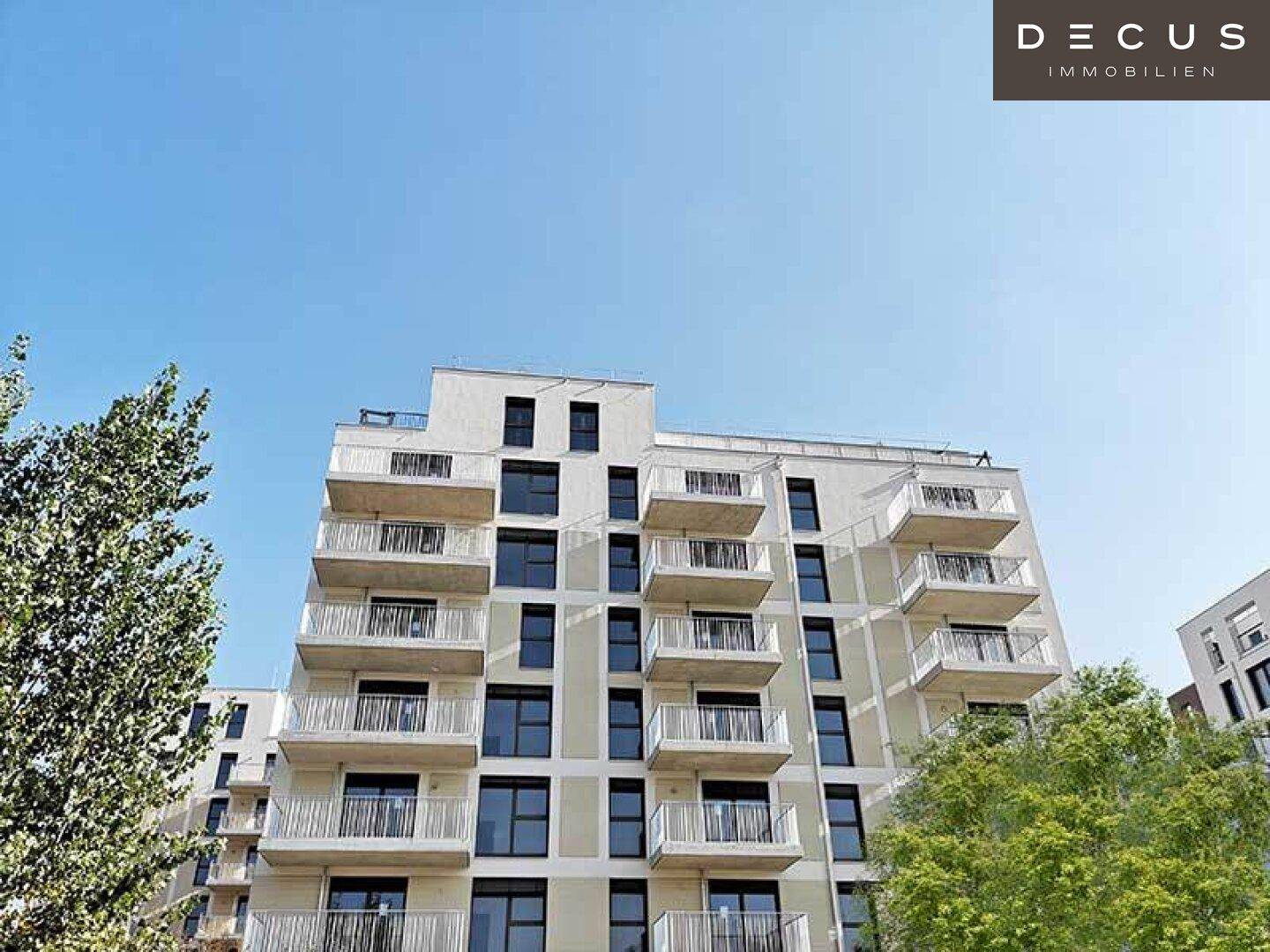 Moderne Wohnanlage mit zahlreichen Balkonen und einer hellen Fassade unter klarem, blauem Himmel.