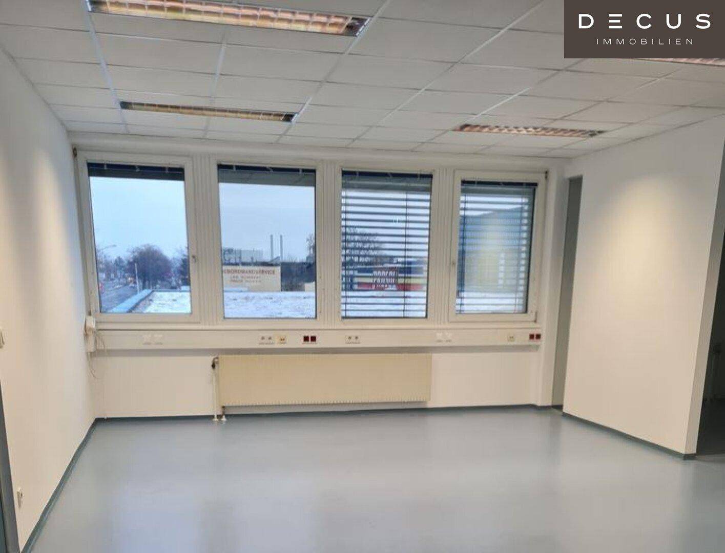 Leeres Büro mit großen Fenstern, Heizkörper und abgehängter Decke, bereit zur Nutzung.