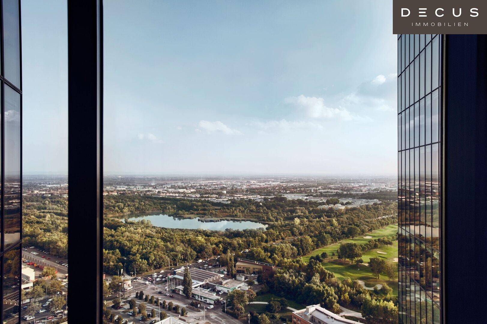 Panoramablick aus einem Hochhausfenster auf eine weite Landschaft mit See und viel Grün.