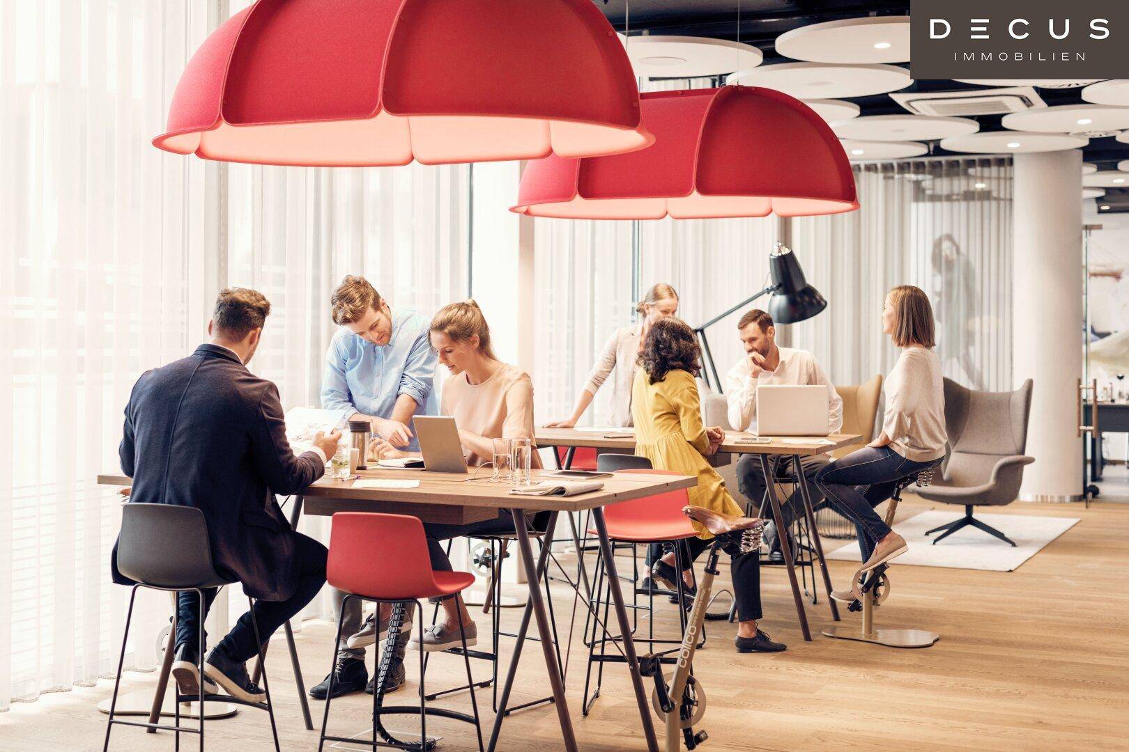 Offener Bürobereich mit modernen Arbeitsplätzen, hohen Tischen und auffälligen roten Lampen.
