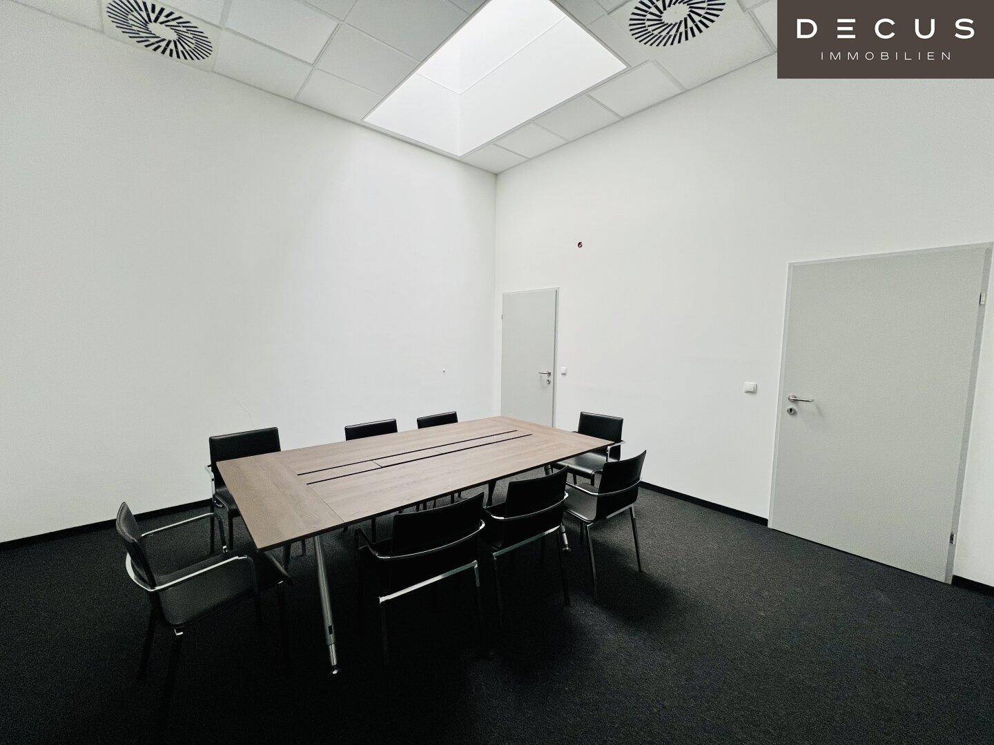 Konferenzraum mit großem Tisch und Stühlen, Teppichboden und Deckenbeleuchtung für Besprechungen.