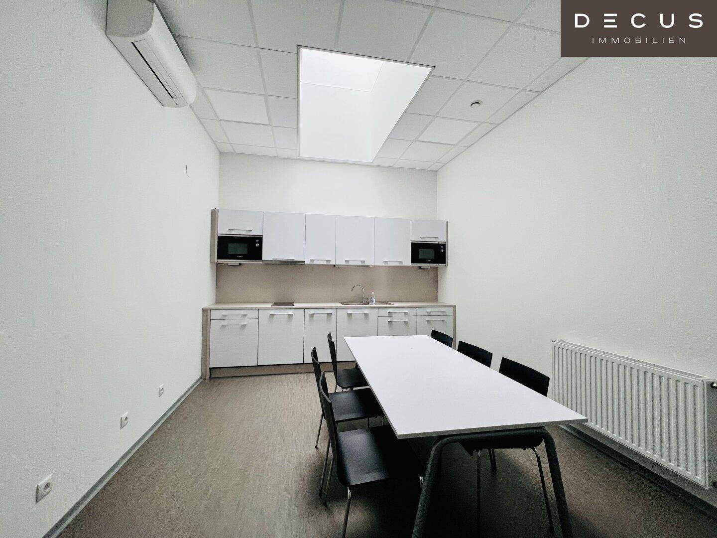 Moderne Teeküche mit weißen Schränken, integrierten Mikrowellen und Essbereich für Mitarbeiter.