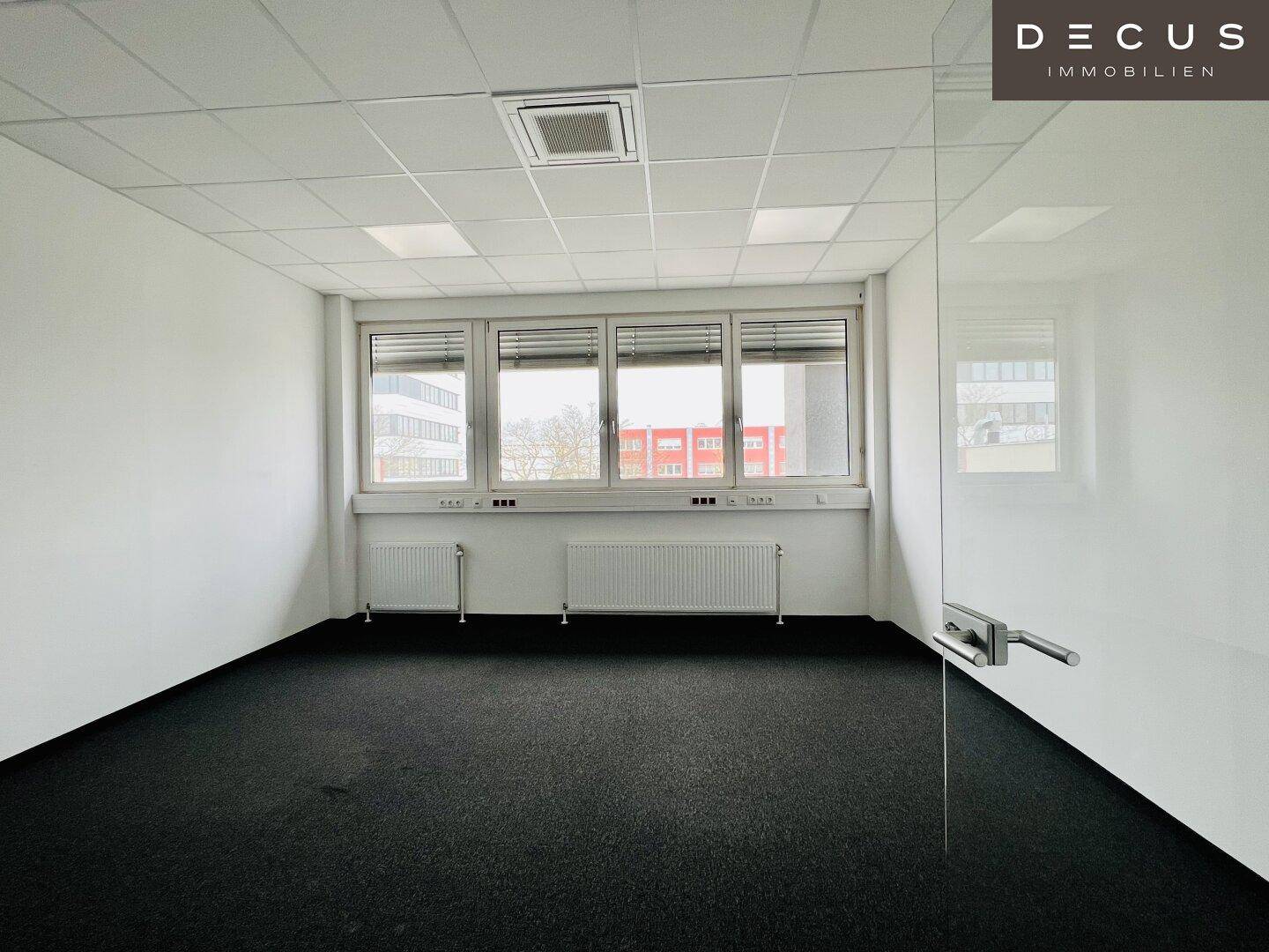 Helles Büro mit Teppichboden, großen Fenstern und einer modernen Glasabtrennung, die den Raum strukturiert.