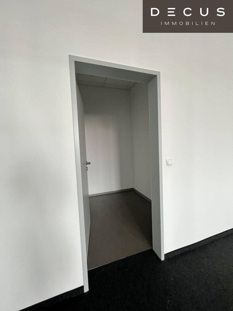 Eingang zu einem kleinen Abstellraum mit dunklem Bodenbelag und weißen Wänden.