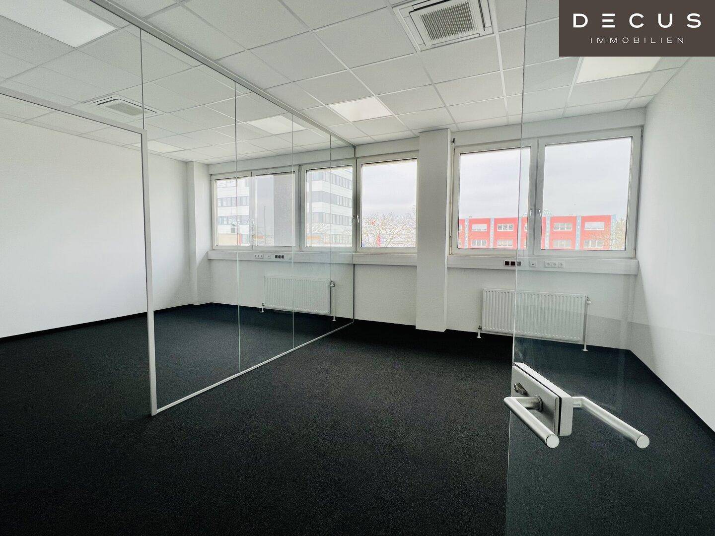 Großes Büro mit Teppichboden, vielen Fenstern und mehreren Glaswänden für eine offene Raumgestaltung.