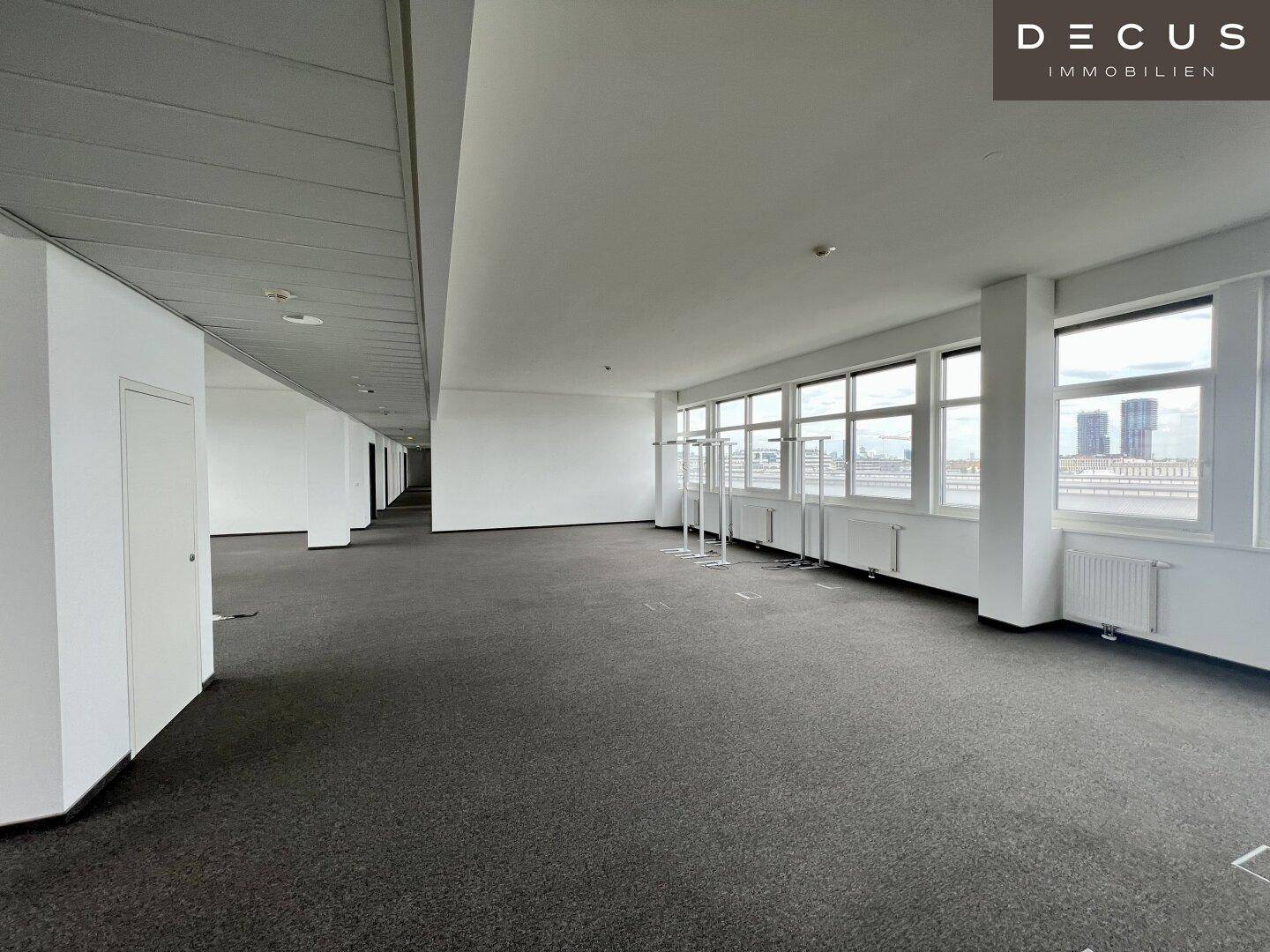 Weitläufiger Bürobereich mit Teppichboden, großen Fenstern und Blick auf die Umgebung.