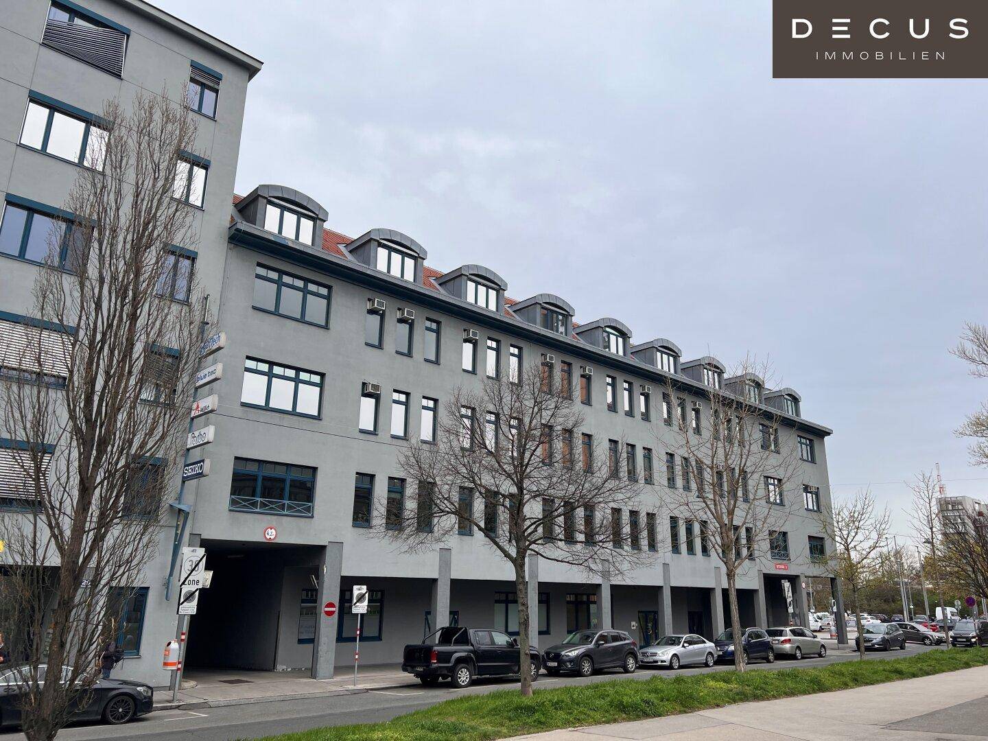 Seitenansicht eines modernen Bürogebäudes mit mehreren Etagen und parkenden Autos entlang der Straße.