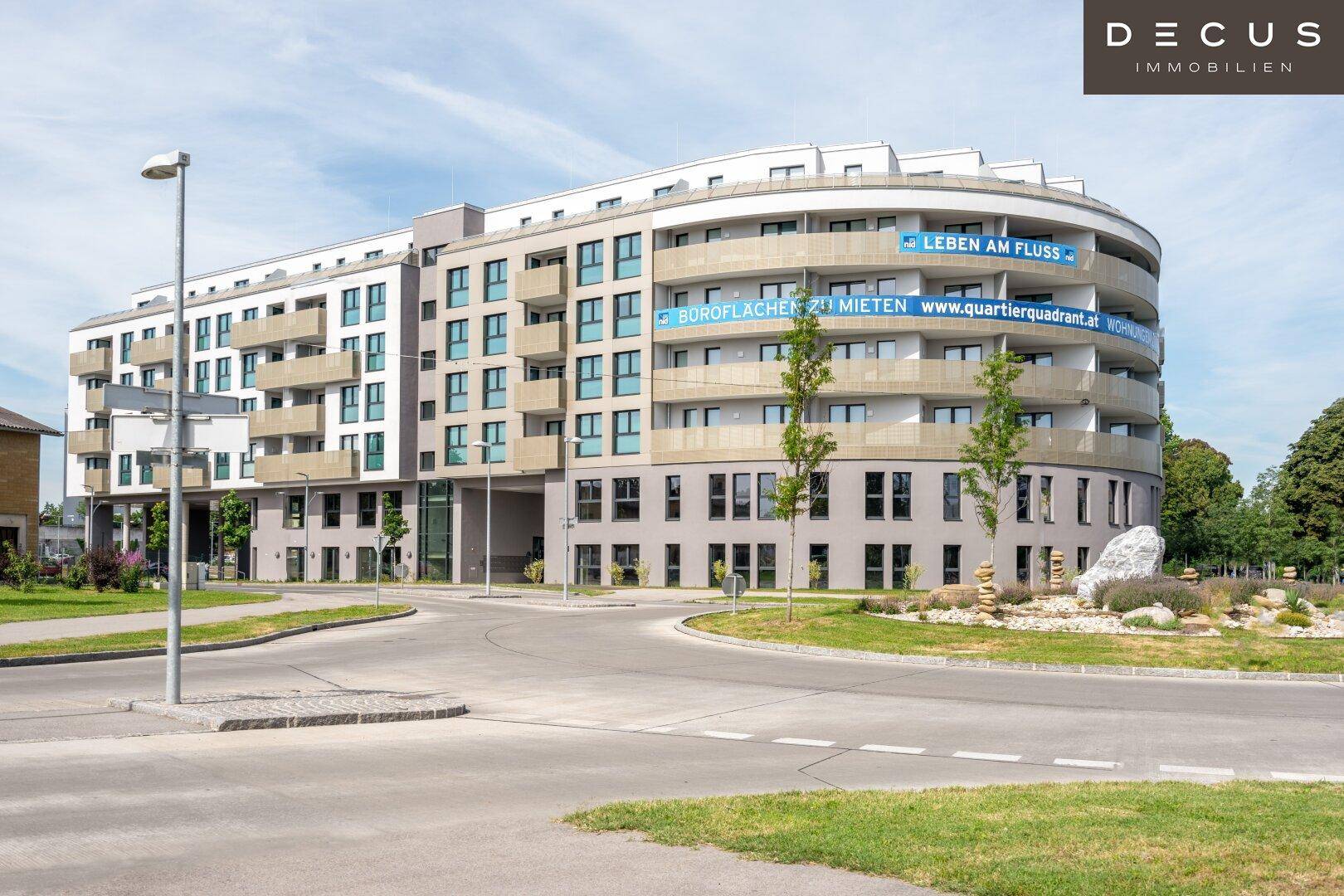 Ansicht des modernen Apartmentgebäudes von der Straße mit geschwungener Fassade und umliegender Landschaftsgestaltung.