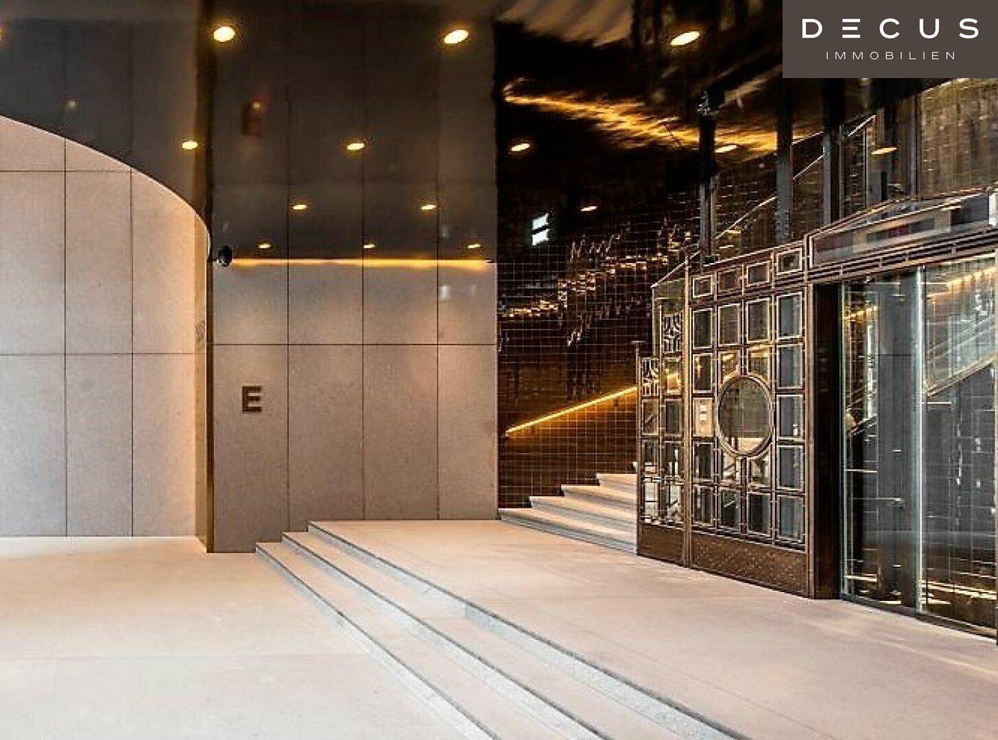 Moderner Eingangsbereich mit dunklen Hochglanzflächen, Treppen und einem dekorativen Aufzug.