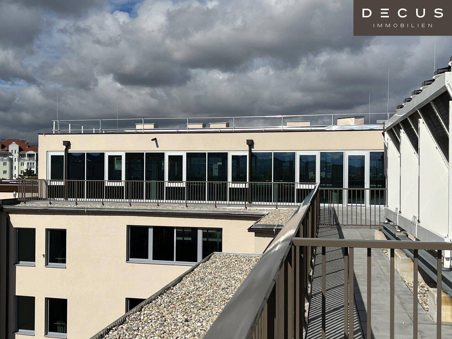 Dachbereich eines Gebäudes mit Kiesbelag und einer Reihe von Fenstern unter bewölktem Himmel.